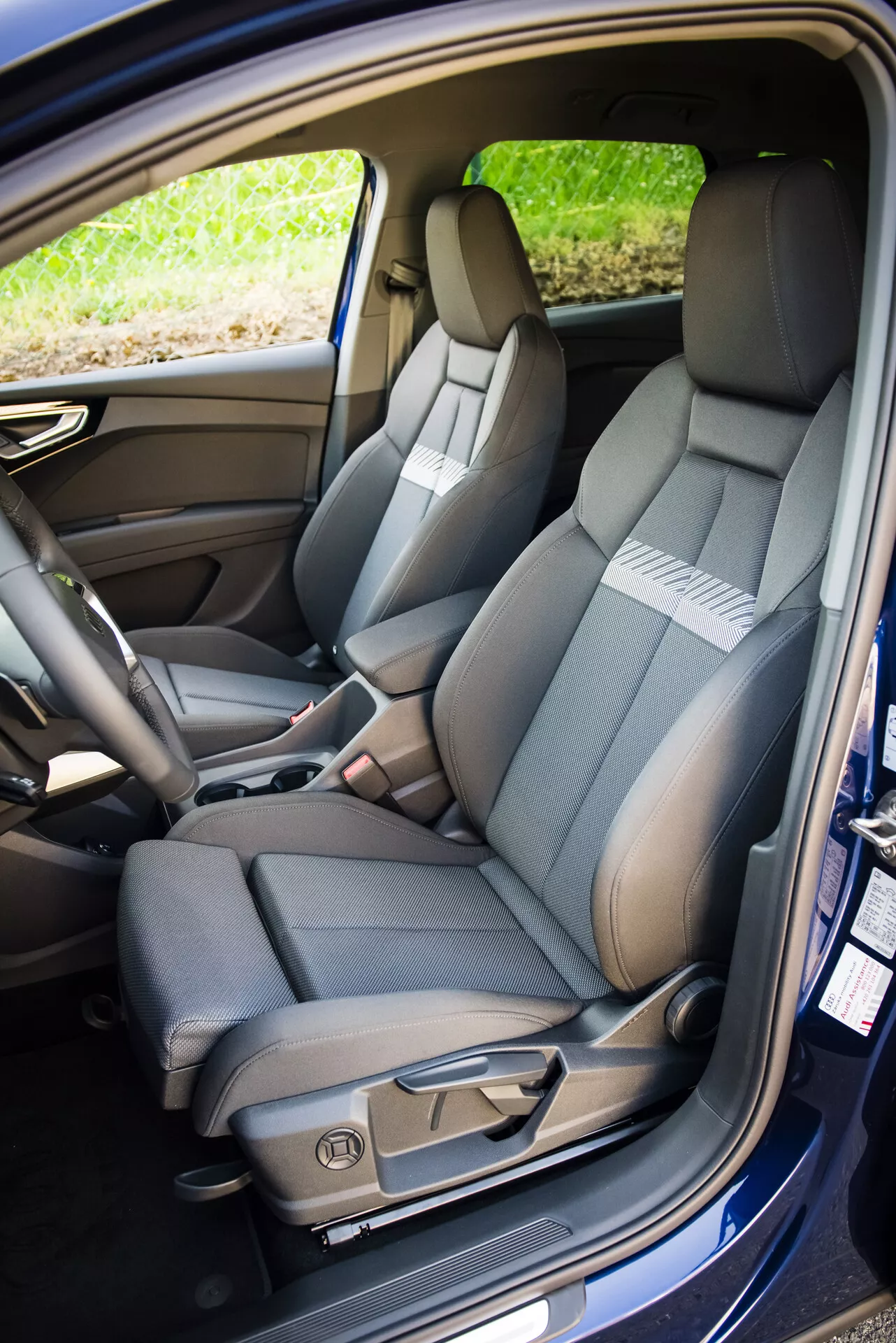 Interior del Audi Q4 e-tron 2021 mostrando el asiento delantero del lado del pasajero con tapicería bicolor, costuras detalladas, controles de ajuste eléctrico y cinturón de seguridad, junto con una visión del asiento trasero abatible partido y características tecnológicas de la cabina.