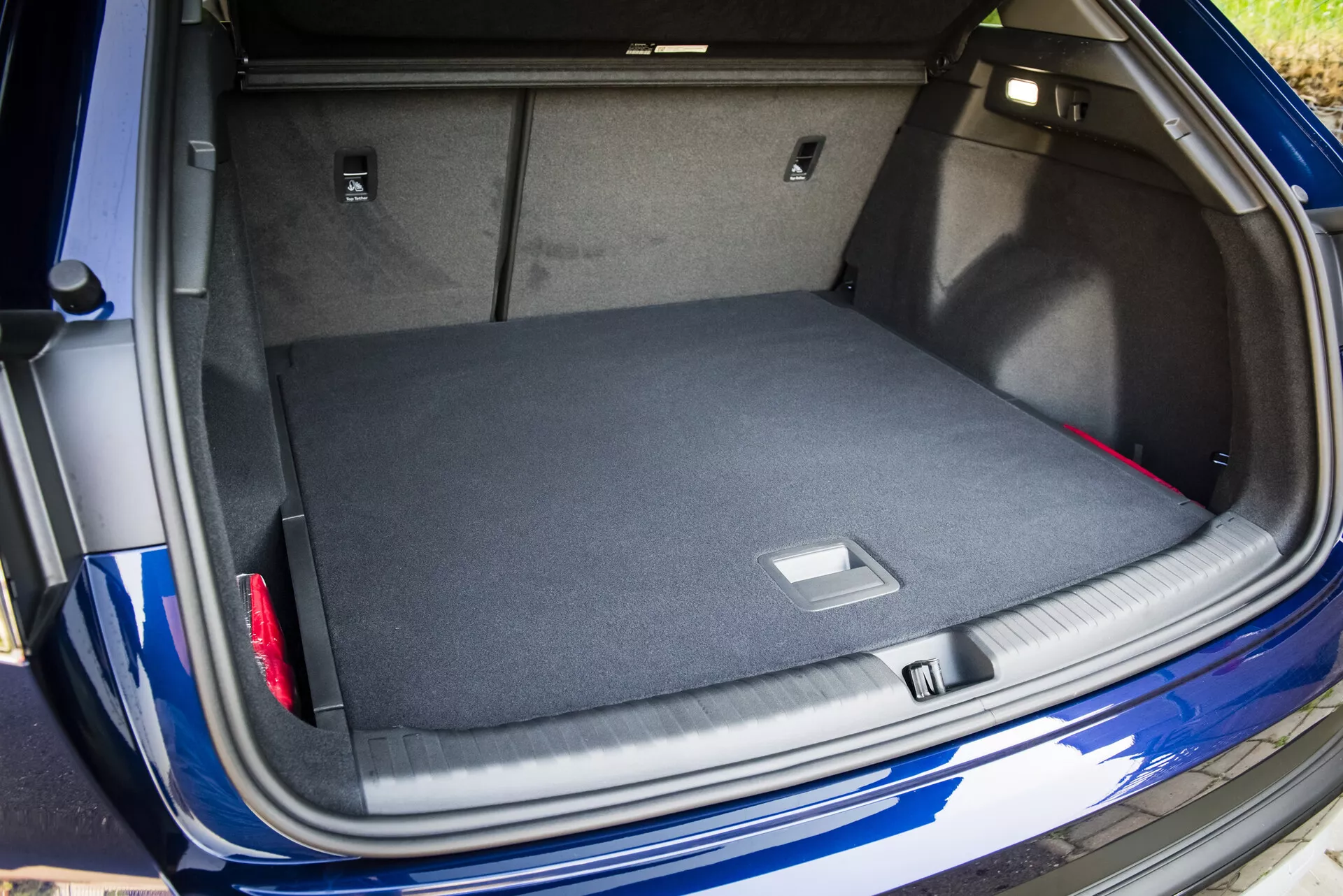 Vista del espacioso maletero alfombrado del Audi Q4 e-tron 2021 con la tapa del maletero abierta, mostrando soluciones de almacenamiento inteligentes y un vistazo a su exterior azul metálico con sensor de estacionamiento visible