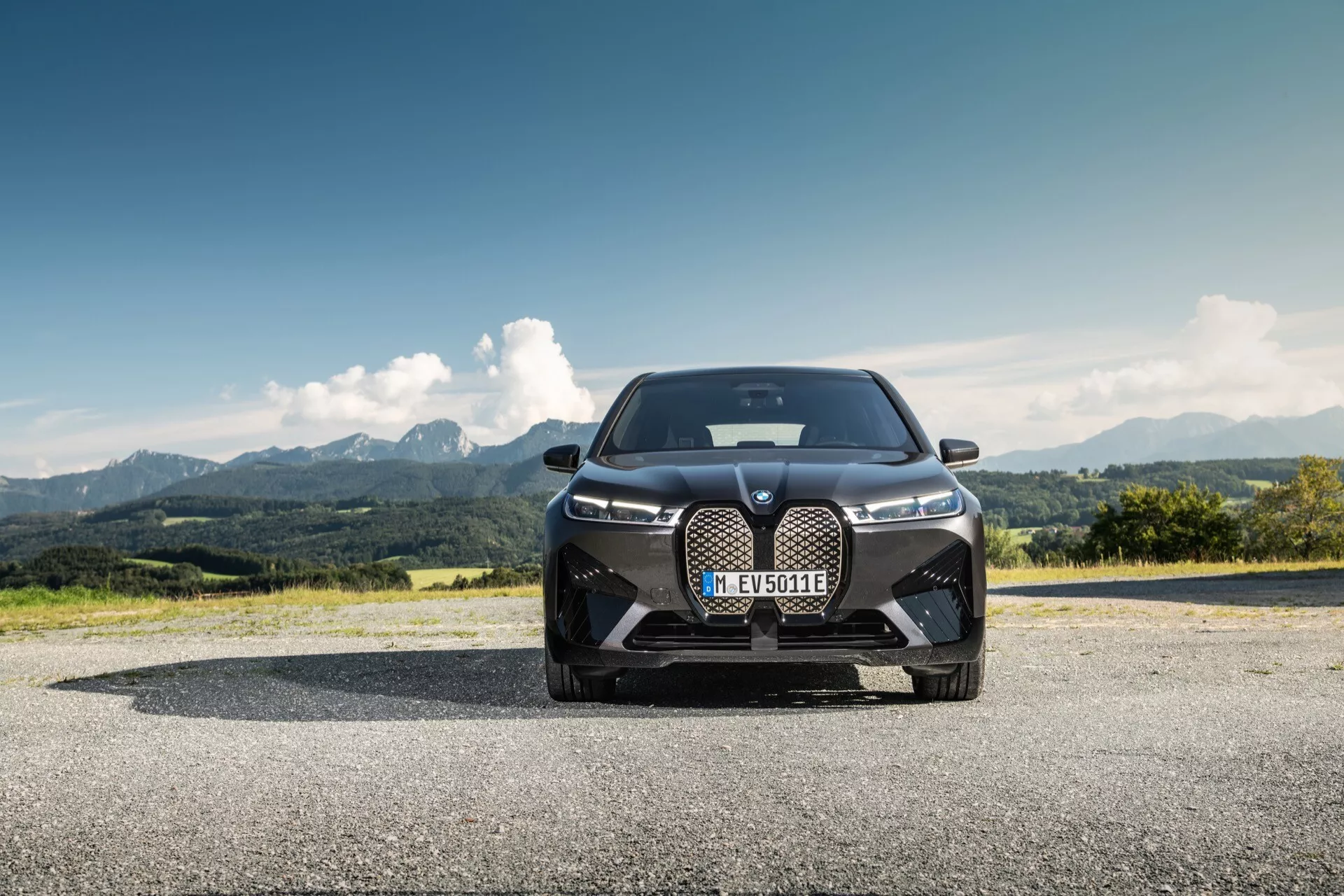 BMW iX (i20) 2021 fotografiado desde un ángulo frontal bajo, destacando su diseño dominante con una gran parrilla en forma de riñón, faros LED estilizados y entradas de aire orientadas al rendimiento contra un paisaje montañoso