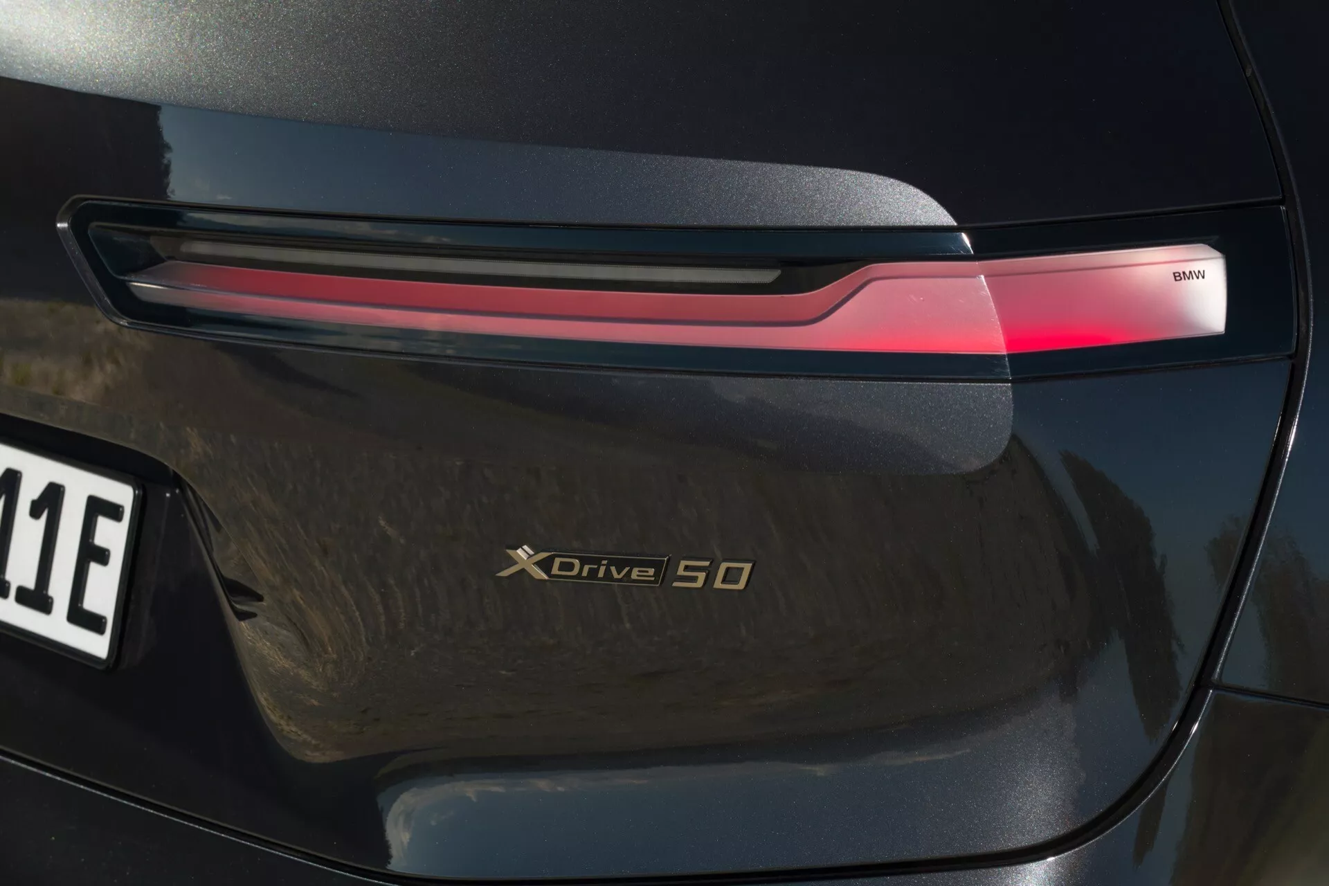 Primer plano de la sección trasera del BMW iX 2021 (i20) destacando la luz trasera LED, el distintivo xDrive 50 y el acabado de alto brillo