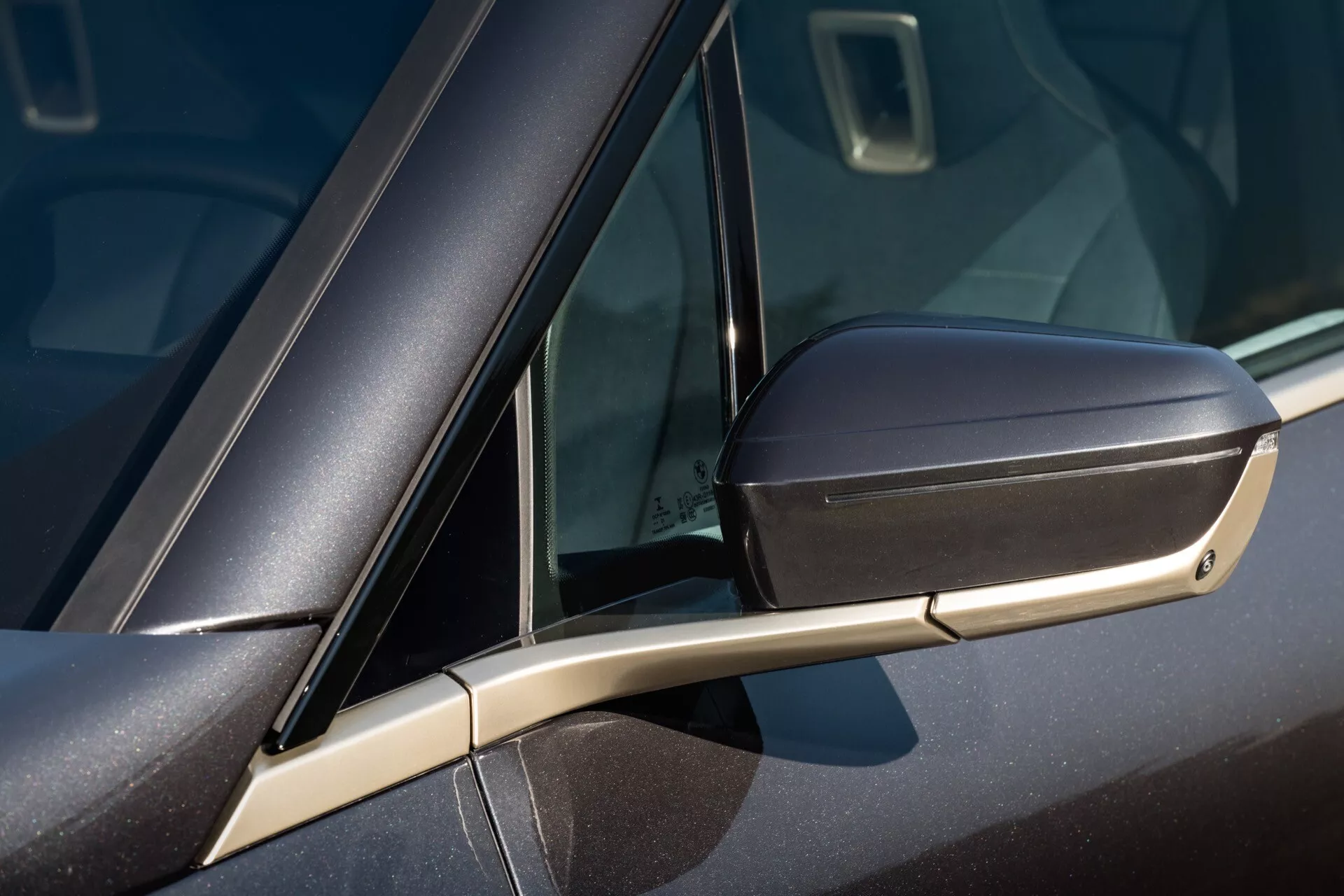 Vista detallada de un BMW iX 2021 (i20) mostrando el espejo lateral a juego con el color del coche con señal de giro integrada, el soporte aerodinámico elegante y una parte de la ventana con el vidrio de cuarto.