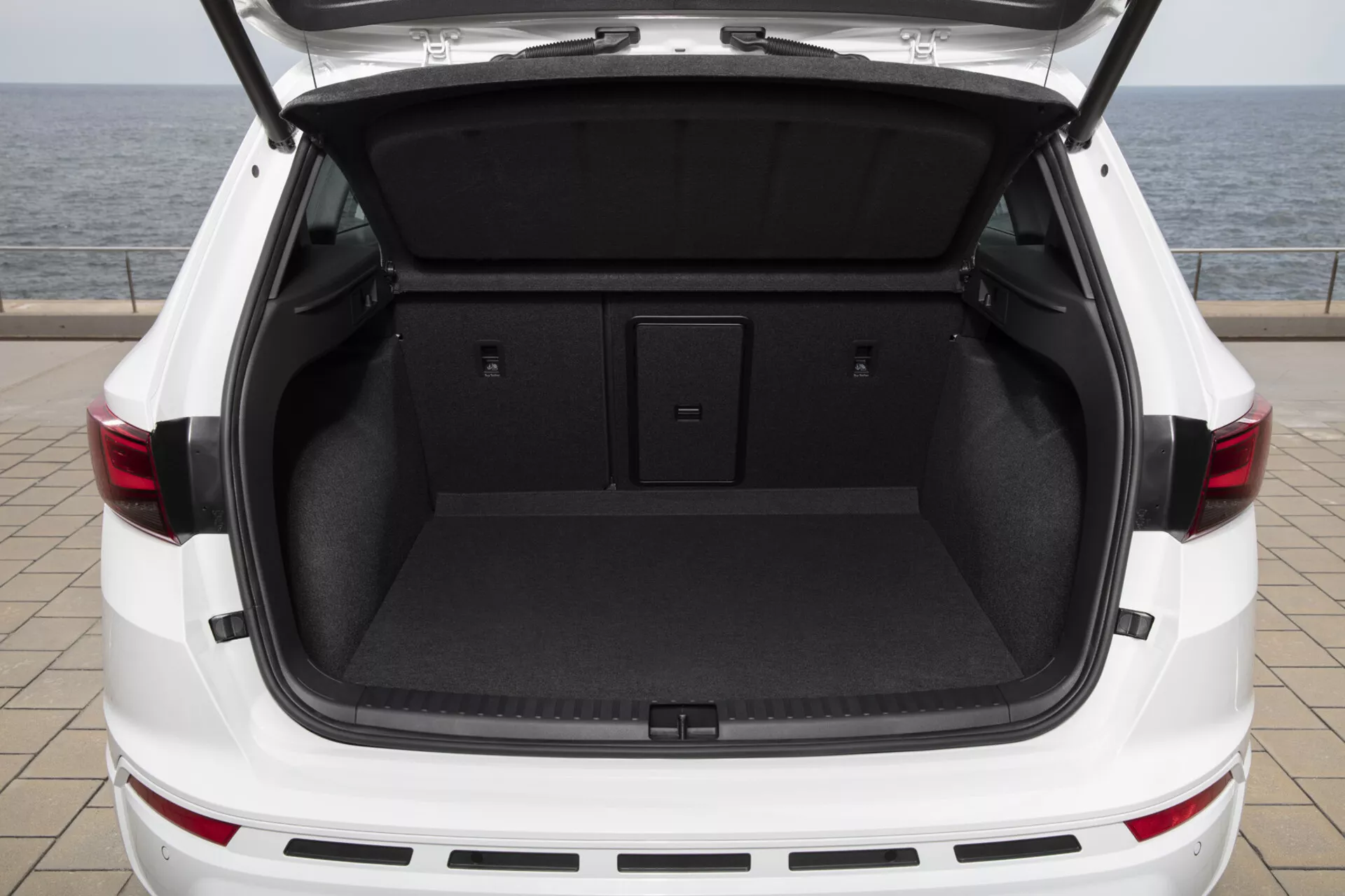 Vista trasera del SUV blanco Cupra Ateca 2020 con el maletero abierto mostrando un área de carga espaciosa y limpia con piso de carga plano y alfombra interior oscura, insinuando características de portón trasero operado por energía y diseño de luces traseras LED.