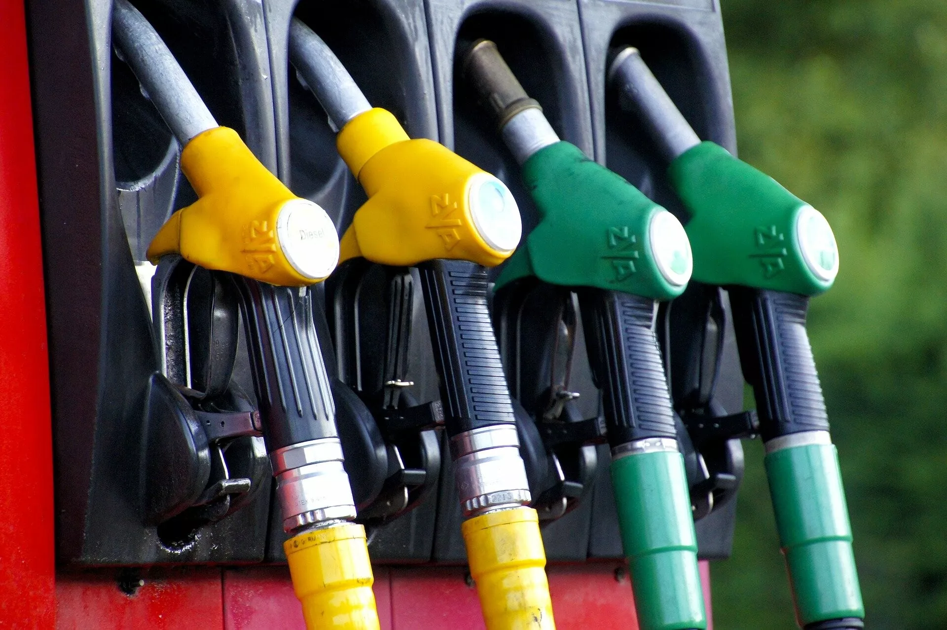 Imagen que muestra un cuarteto de boquillas de bombas de combustible con mangos de colores variados que indican diferentes tipos de combustible, configurado contra un fondo natural suavemente desenfocado, destacando características de diseño y seguridad.