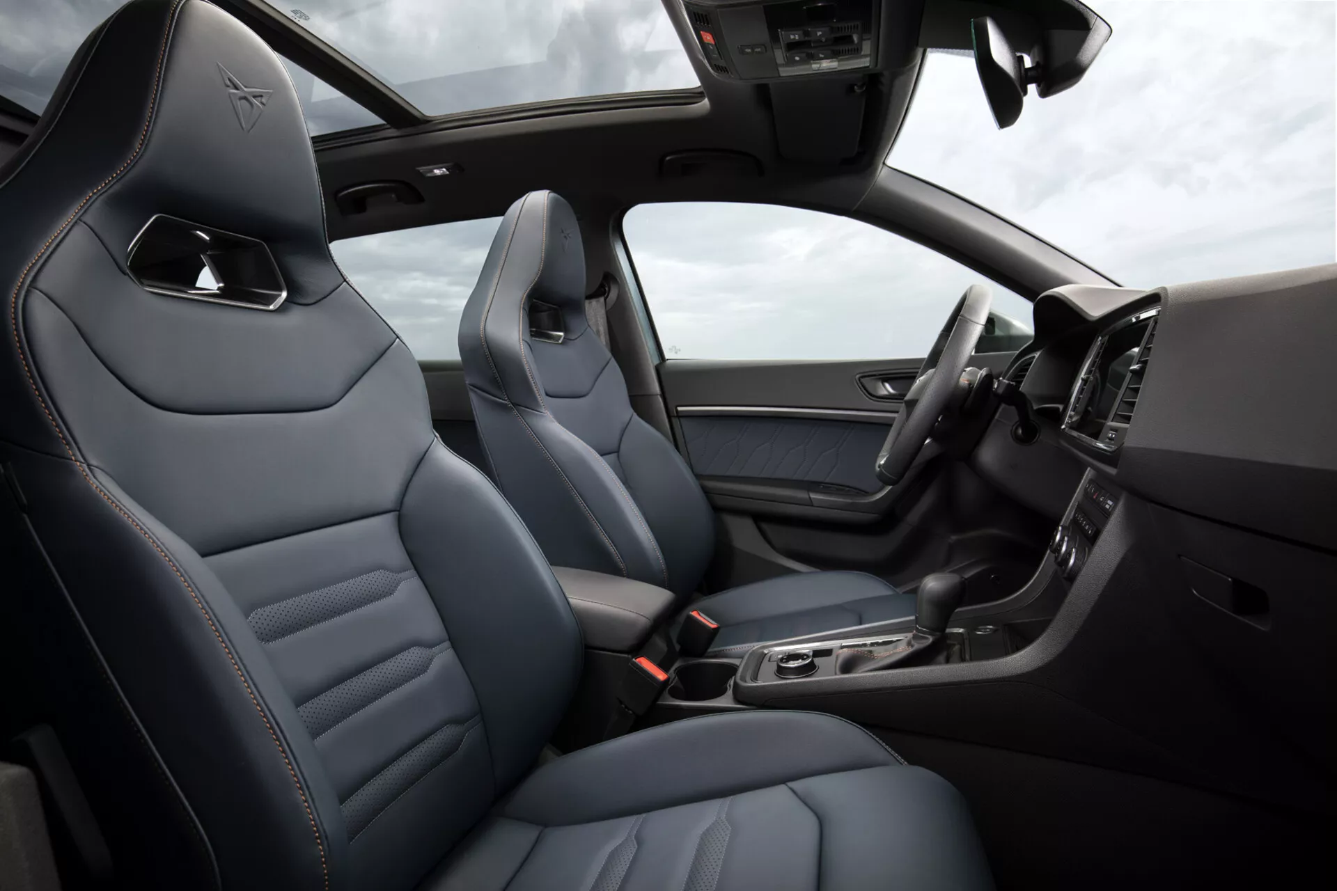 Vista interior del Cupra Ateca 2020, mostrando asientos de cuero de lujo con costuras de diamante, consola central elegante con características tecnológicas, pantalla digital en el tablero y parte del volante con controles, bajo un techo solar iluminado
