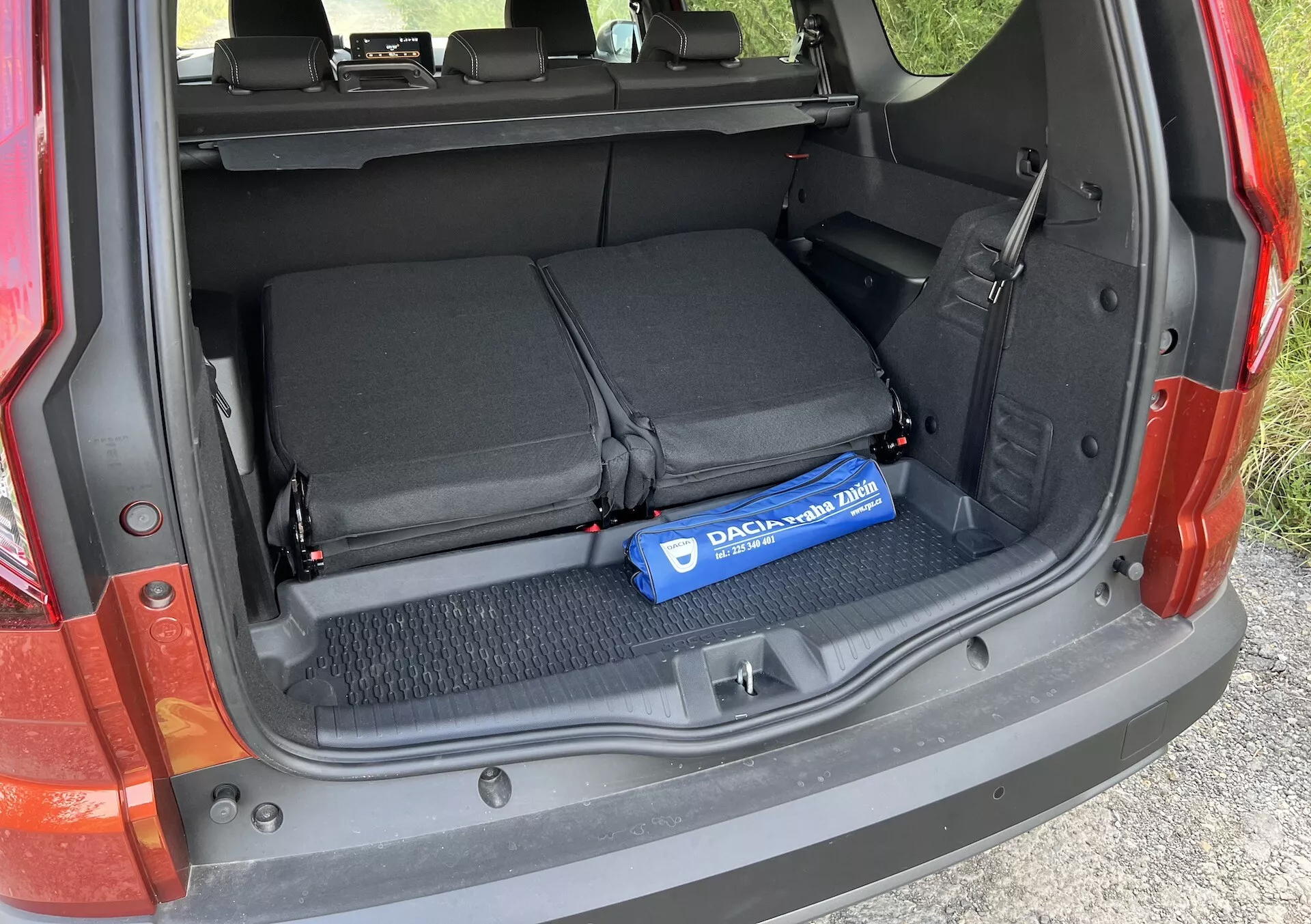 Detalle del maletero del Dacia Jogger 2022 mostrando el área de carga abierta con los asientos traseros abatidos, lazos textiles para asegurar objetos y un cilindro azul Decaux en el suelo alfombrado