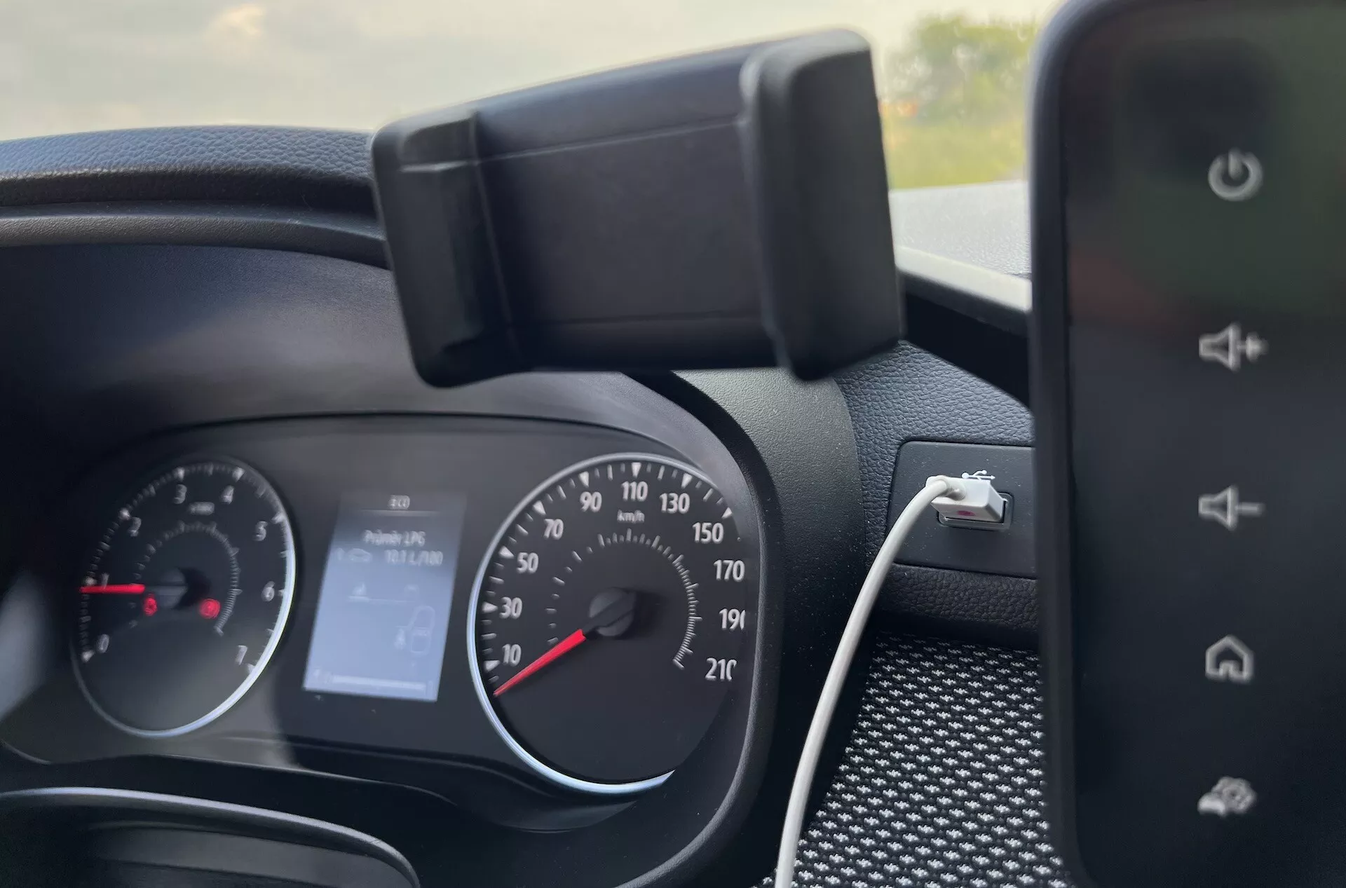 Vista interior detallada del tablero de Dacia Jogger 2022 mostrando el cuadro de instrumentos, controles en el volante y parte del sistema de infoentretenimiento, indicando características como velocímetro estilo análogo, tacómetro, pantalla digital para 'Sin Audio' y capacidades de carga de smartphone.