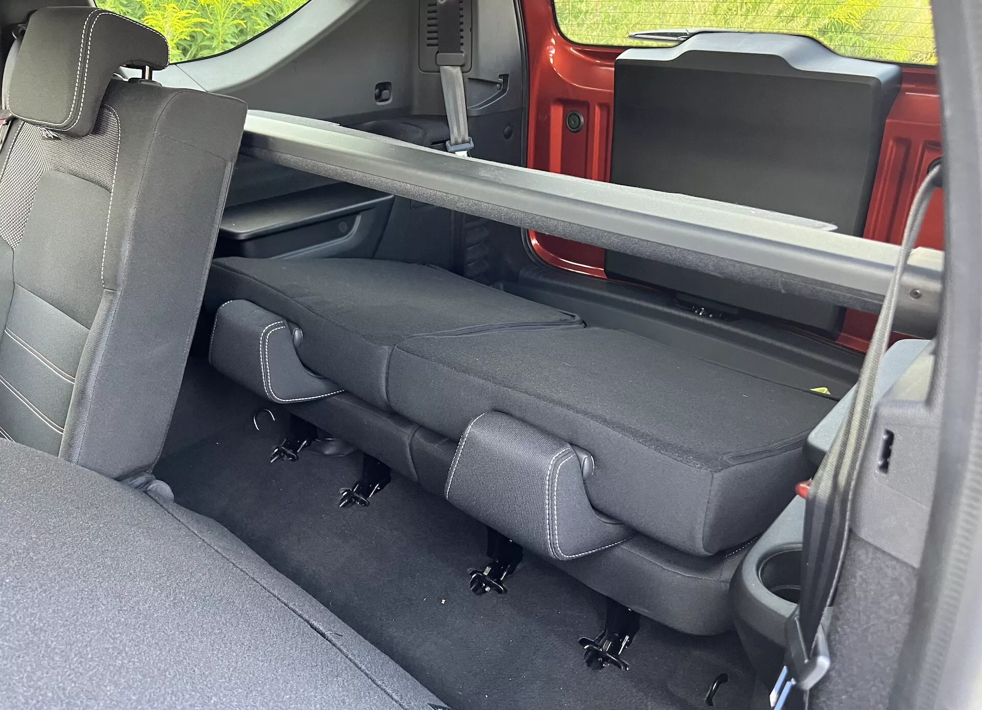 Vista interior del Dacia Jogger 2022 centrada en el compartimento trasero para pasajeros con tapicería oscura, cinturones de seguridad retráctiles, sistema LATCH y mecanismo de asientos plegables visto desde la puerta trasera del lado del pasajero.