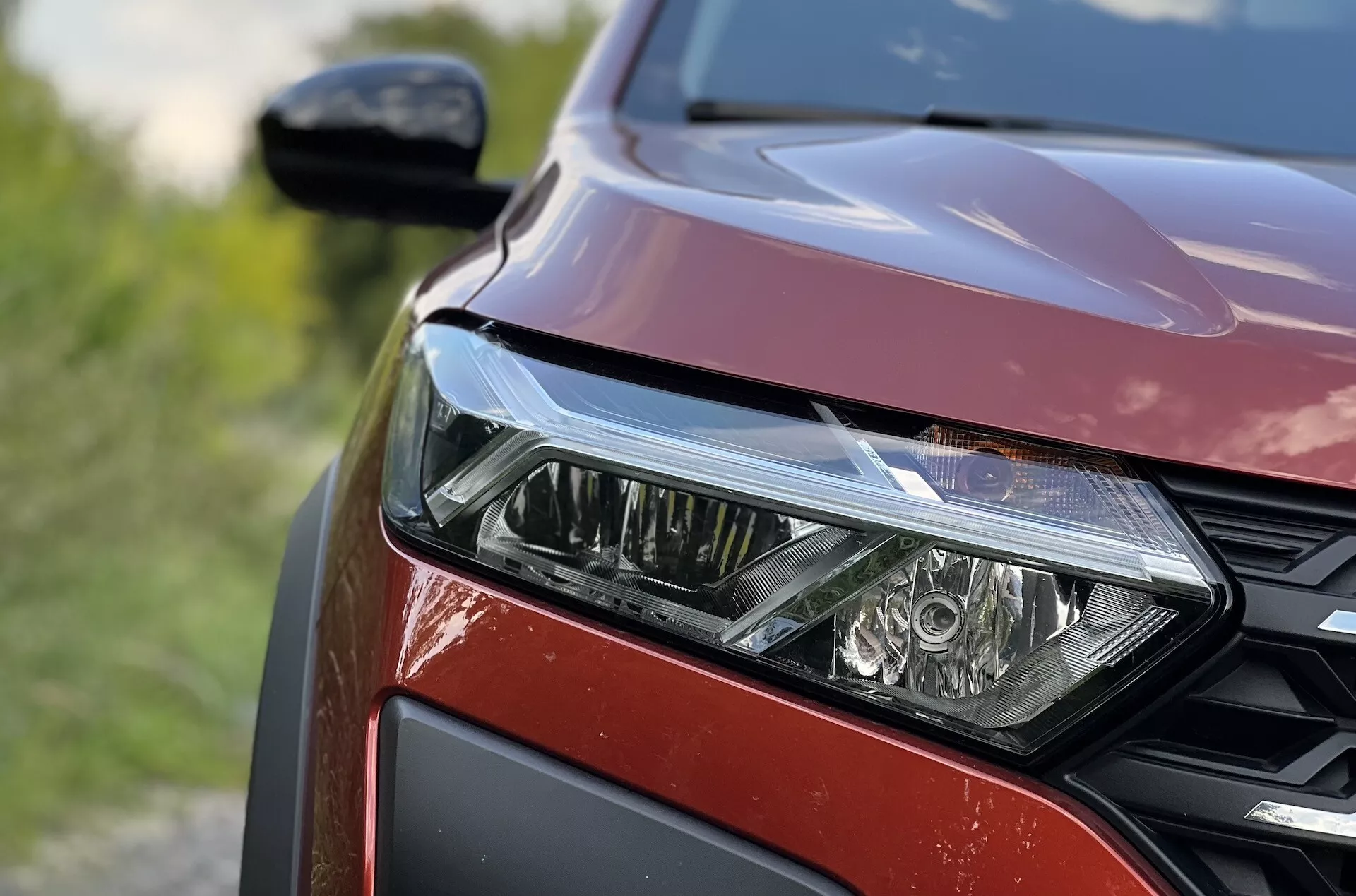 Vista detallada del lado izquierdo delantero del Dacia Jogger 2022 destacando el conjunto de faros LED, patrón de parrilla de panal y acabado de pintura roja metálica