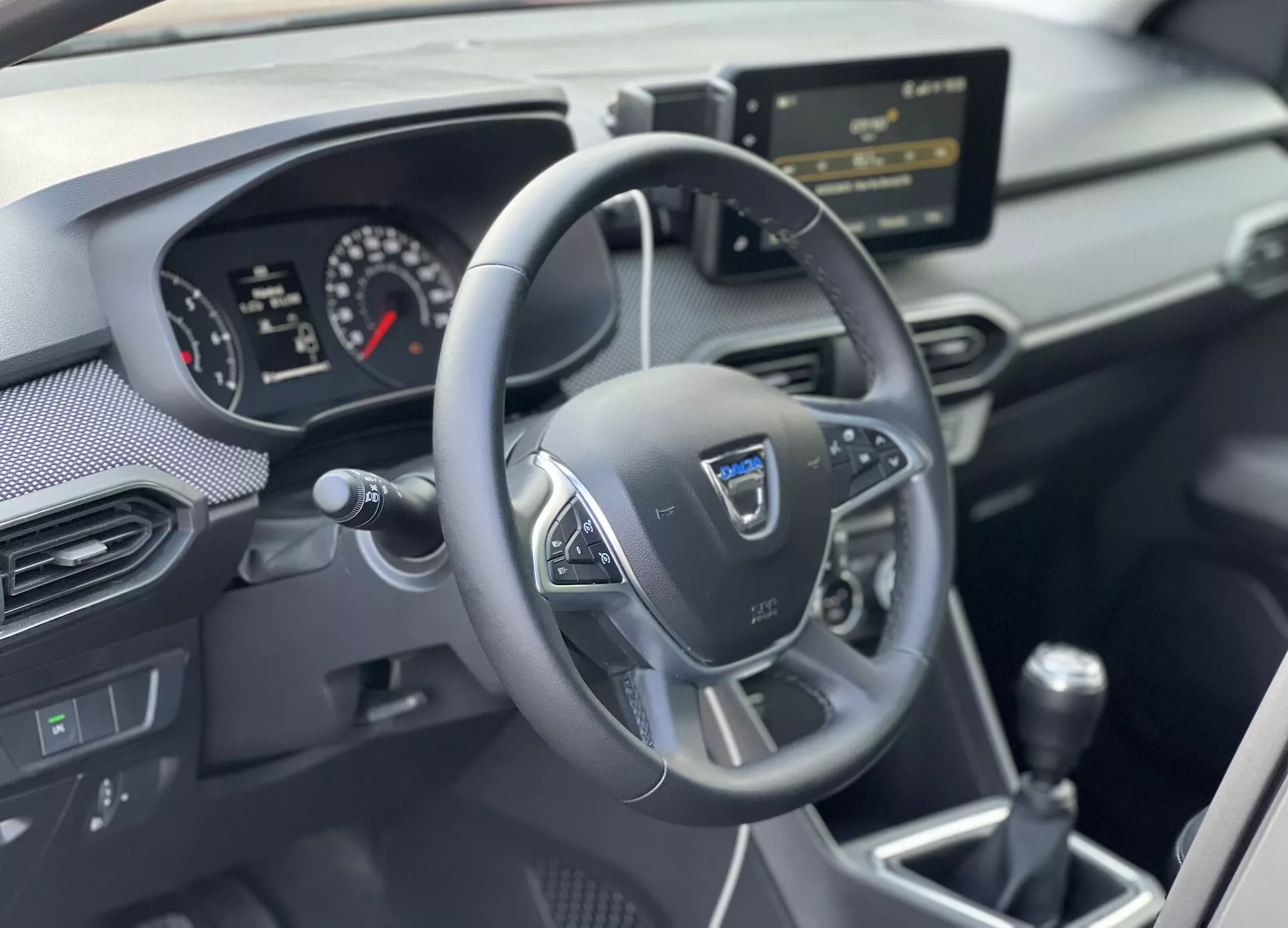 Vista interior del Dacia Jogger 2022 centrada en el área del conductor con volante multifunción de tres radios, cuadro de instrumentos analógico-digital, consola central con sistema de infotenimiento y palanca de cambios manual