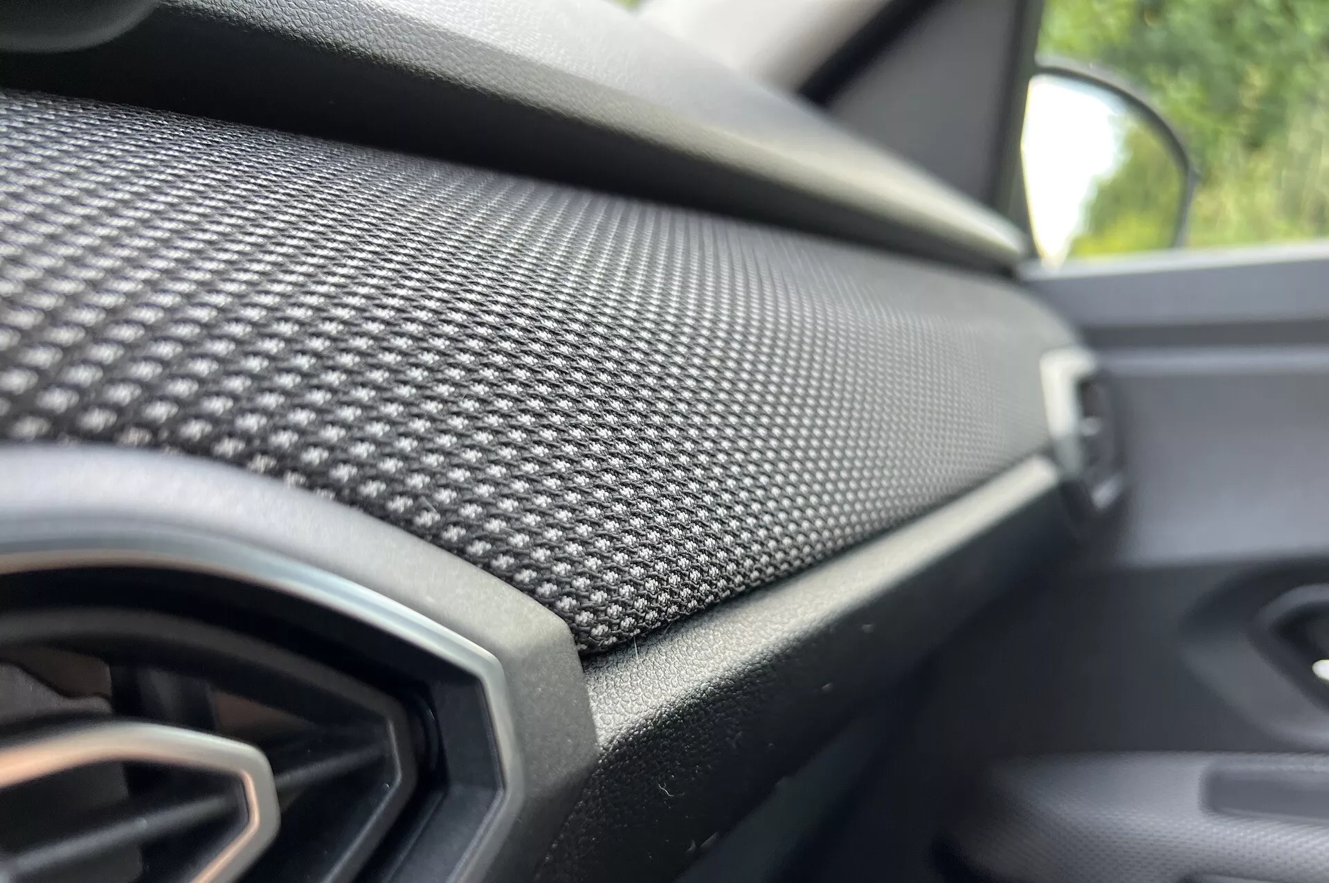 Vista de cerca del tablero del lado del pasajero del Dacia Jogger 2022 con patrón de fibra de carbono y rejilla de ventilación, enfatizando el diseño moderno y el acabado de lujo