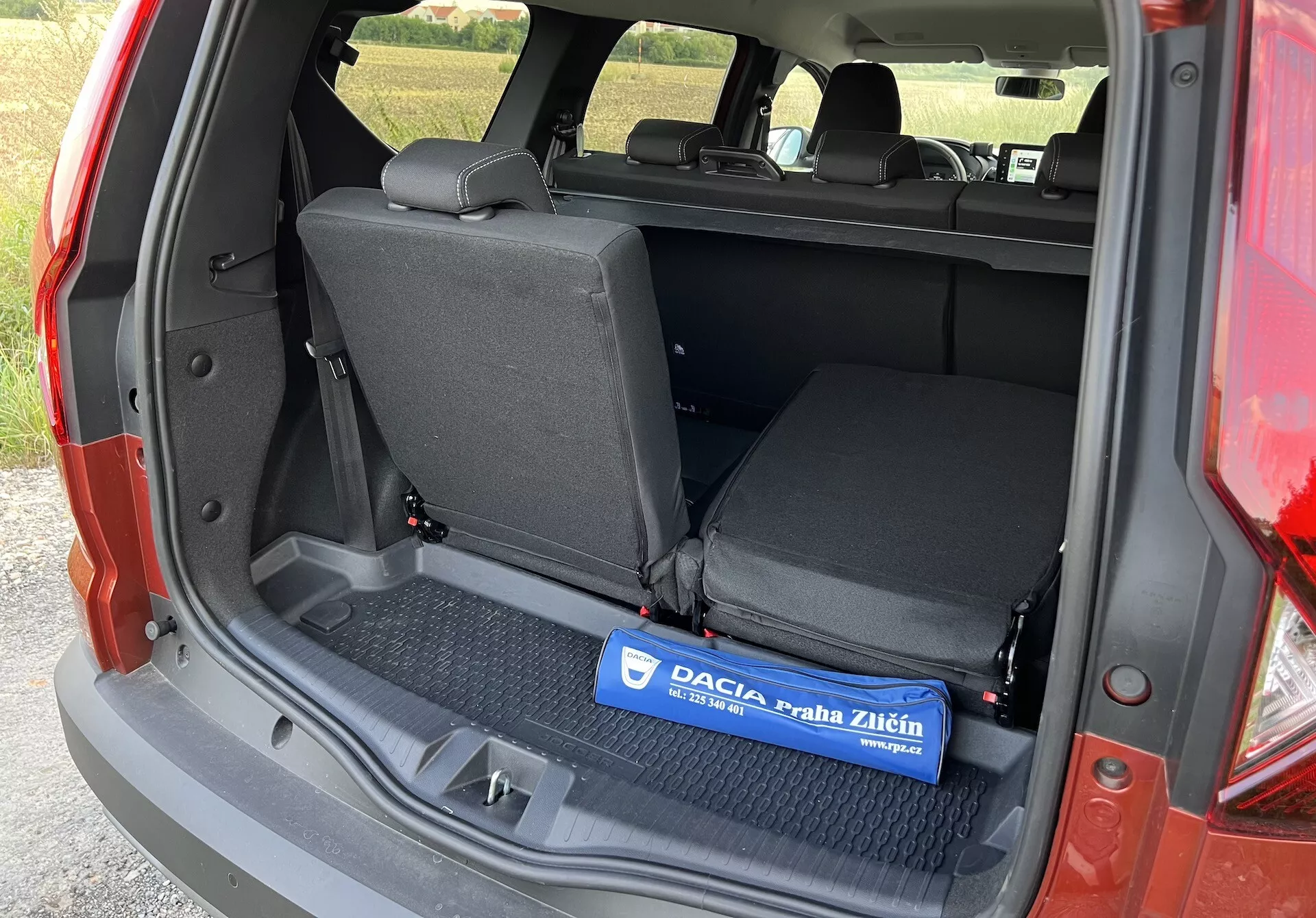 Dacia Jogger 2022 mostrando el espacio de carga interior desde un ángulo lateral izquierdo con el maletero abierto, destacando una zona de carga plana con alfombra de caucho, asientos traseros abatibles 60/40 y detalles de molduras laterales sin componentes de tecnología avanzada o lujo visibles