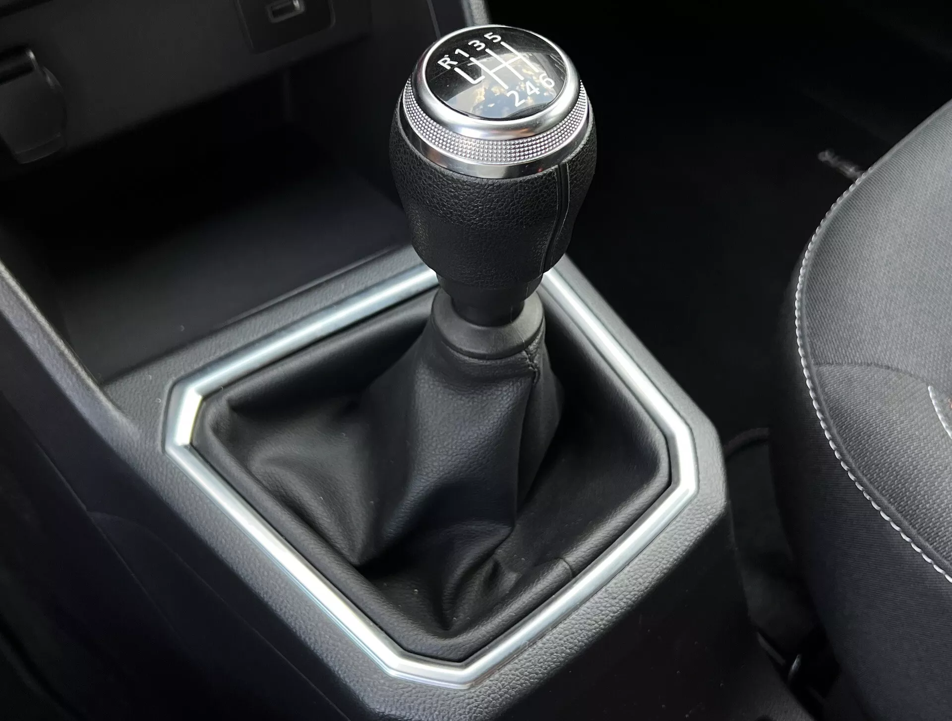 Vista cercana de la palanca de cambios de transmisión manual de Dacia Jogger 2022, mostrando un patrón de cambio de 6 velocidades, palanca cubierta de cuero e inserción metálica hexagonal en un interior de coche refinado