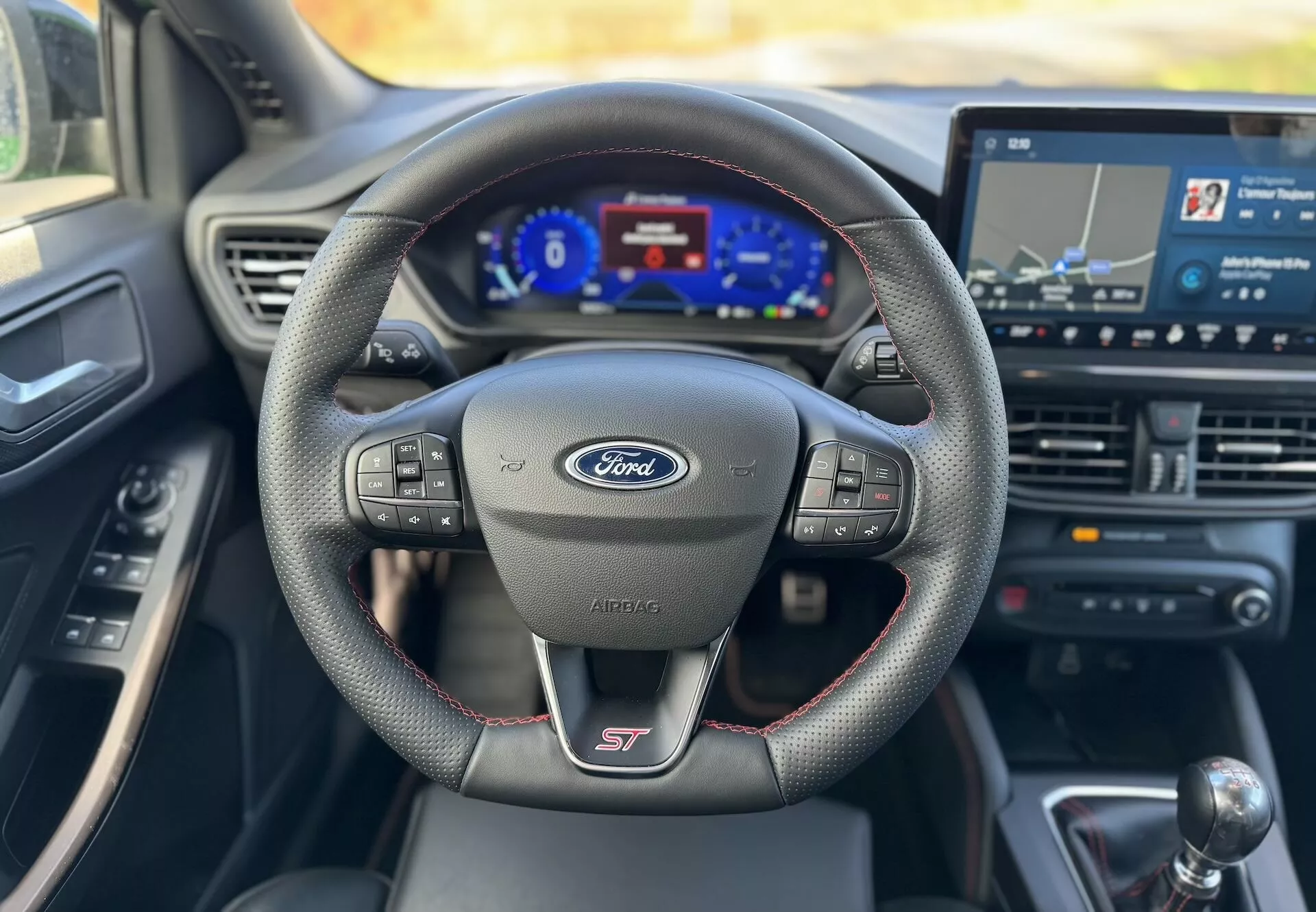 Vista interior del Ford Focus ST 2022 destacando el volante deportivo multifuncional con logo del fabricante y designación del modelo, cuadro de instrumentos digital y sistema de infoentretenimiento táctil con navegación