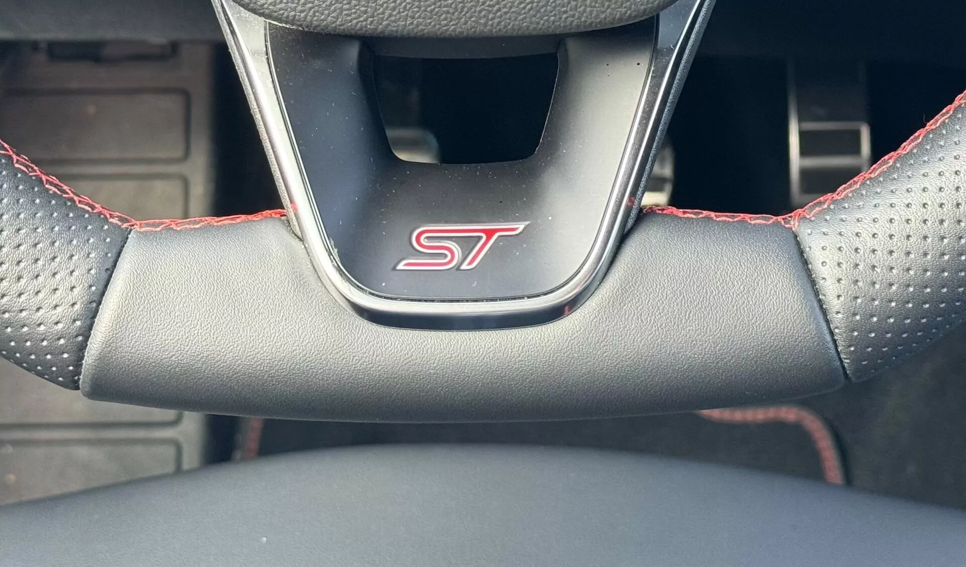Primer plano del volante del Ford Focus ST 2022 destacando la insignia ST, agarre de cuero perforado con costuras rojas, desde la perspectiva del conductor