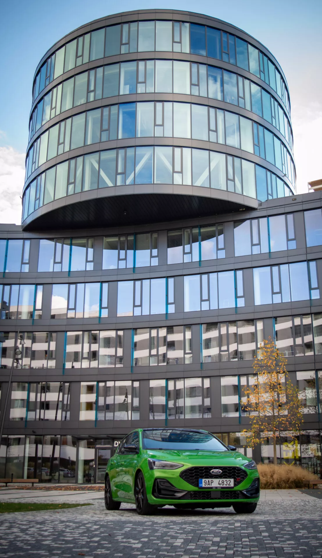 Ford Focus ST 2022 en verde vívido posicionado al aire libre con un edificio de vidrio de fondo mostrando sus elegantes faros, parrilla frontal prominente, ruedas de aleación y diseño aerodinámico