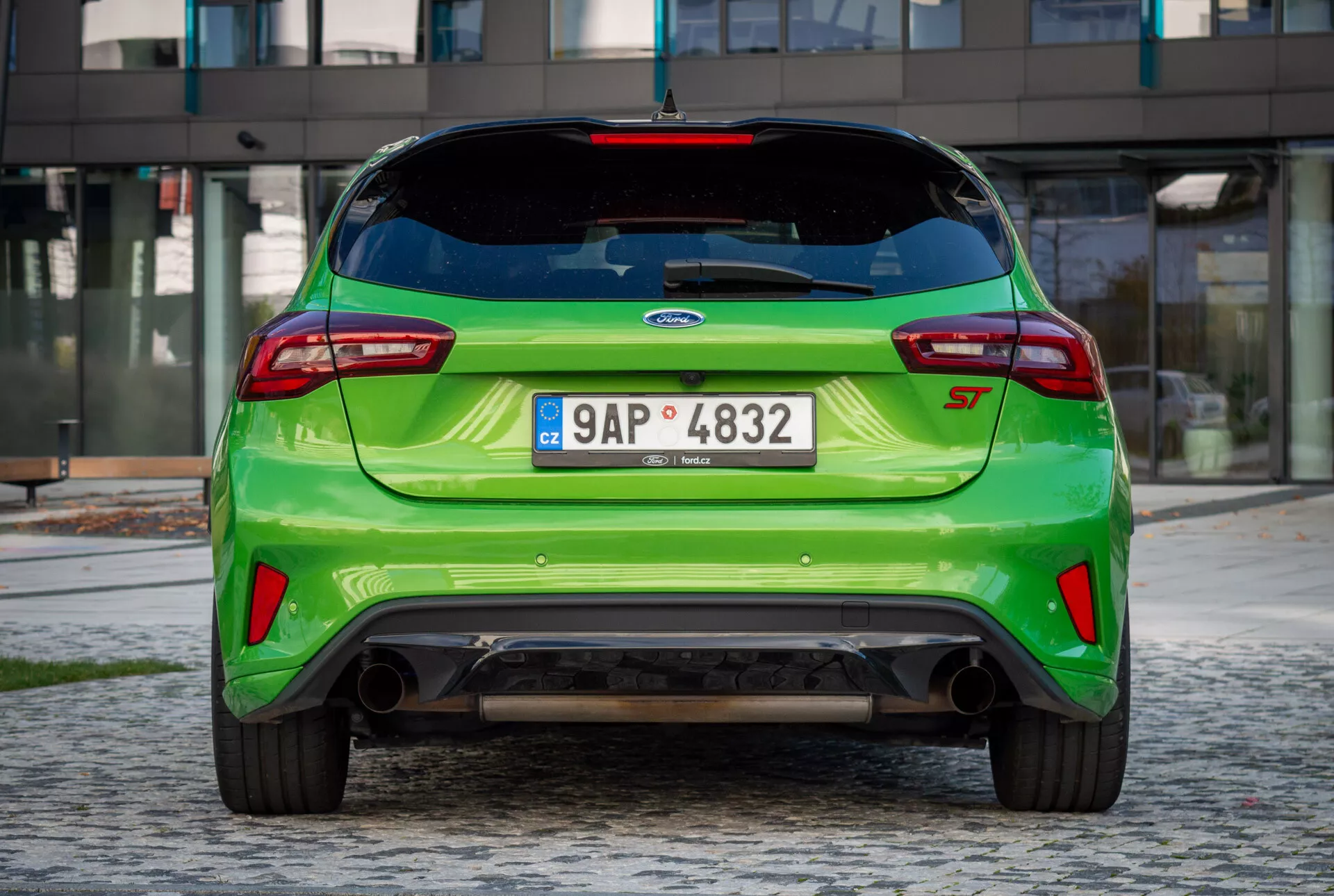 Vista trasera del Ford Fiesta ST 2022 de color verde brillante con spoiler de techo, distintivo EcoBoost, tubos de escape dobles y difusor trasero sobre fondo de adoquines