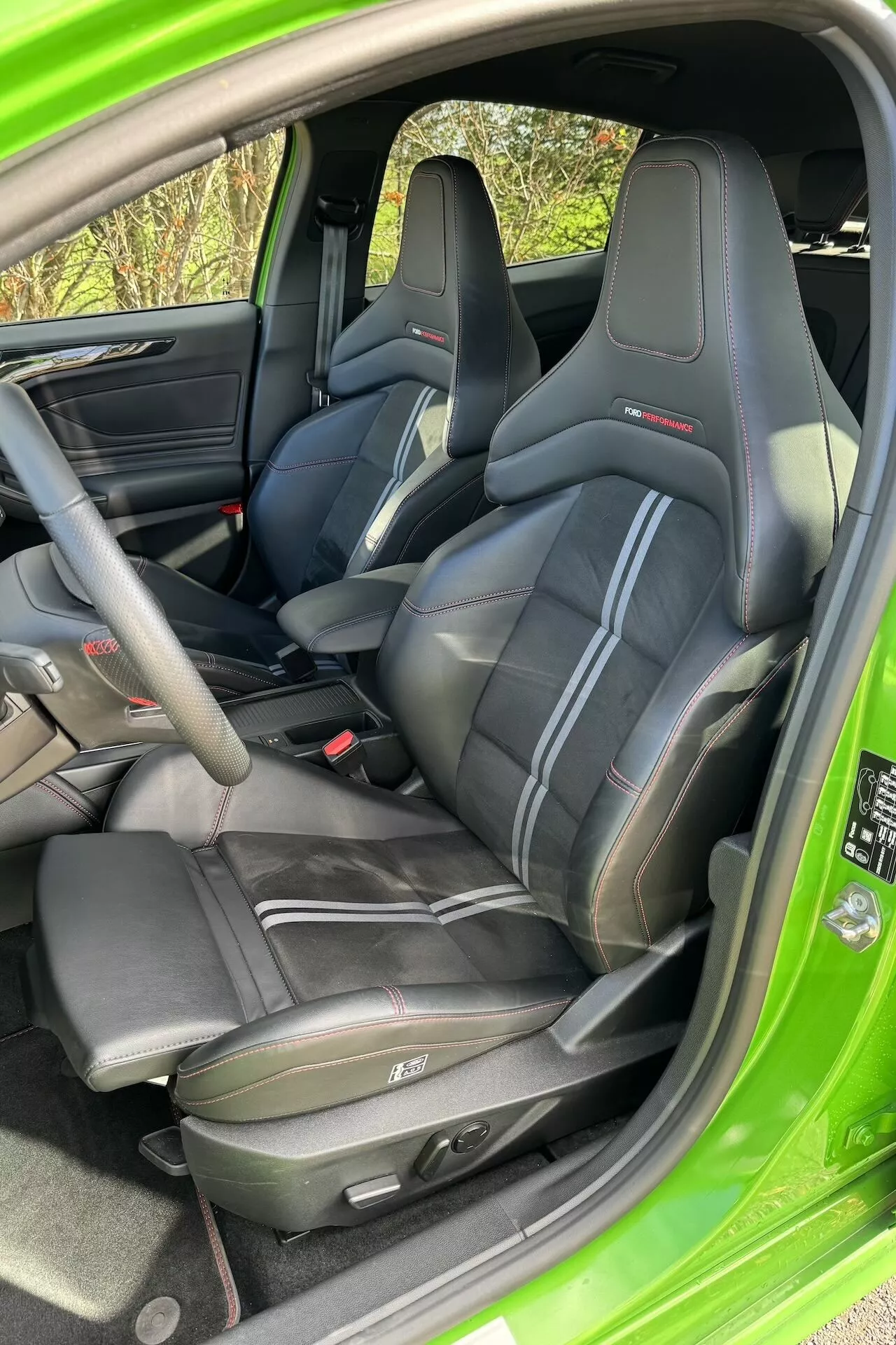 Interior del Ford Focus ST 2022 mostrando asientos tipo baquet de cuero negro con costuras en contraste y reposacabezas integrados, diseño detallado de la puerta y consola central, y luz natural iluminando el vibrante color verde exterior
