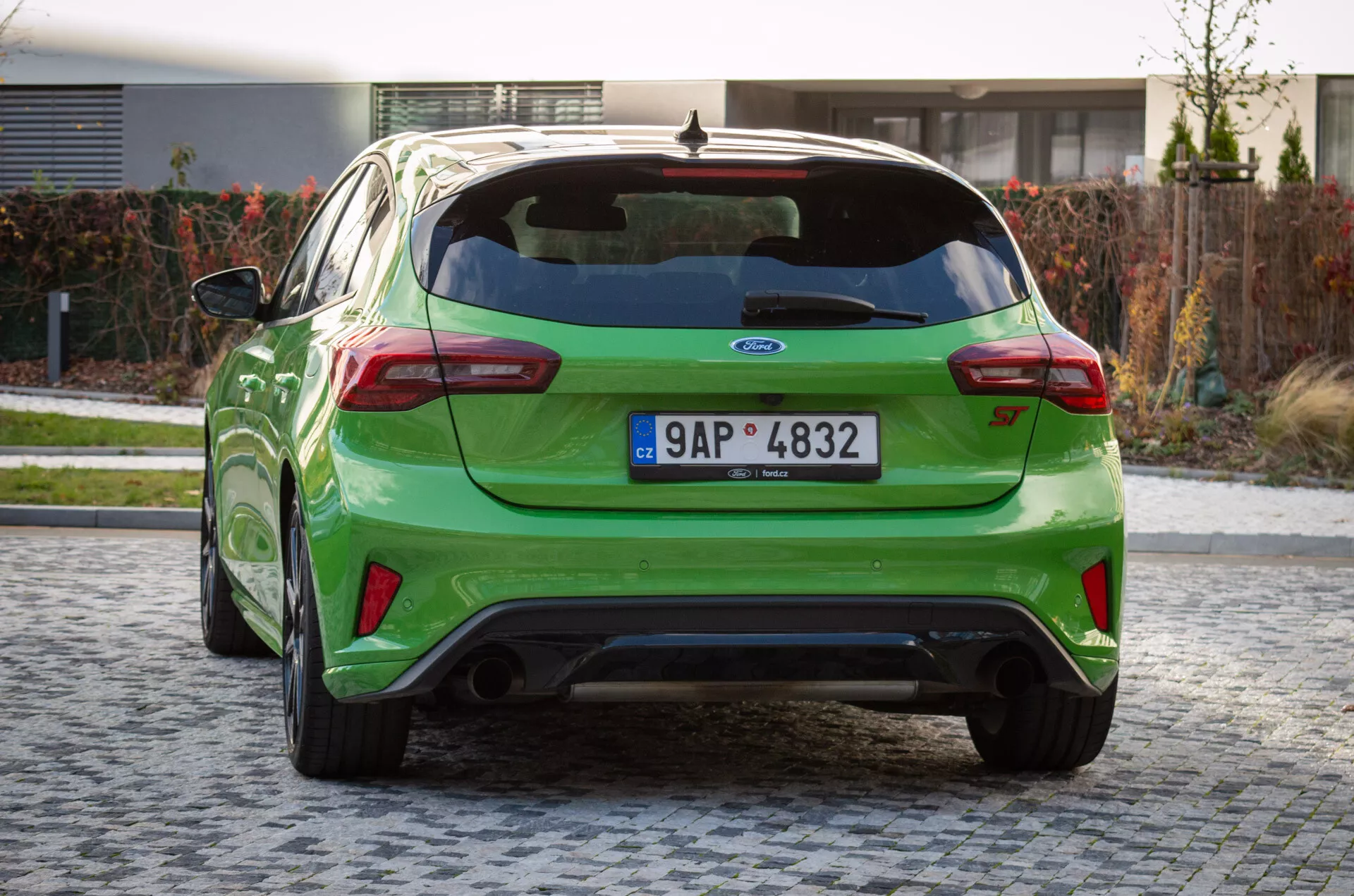 Perspectiva trasera del Ford Focus ST 2022 en verde brillante sobre adoquines, con spoiler, doble escape y emblema del fabricante