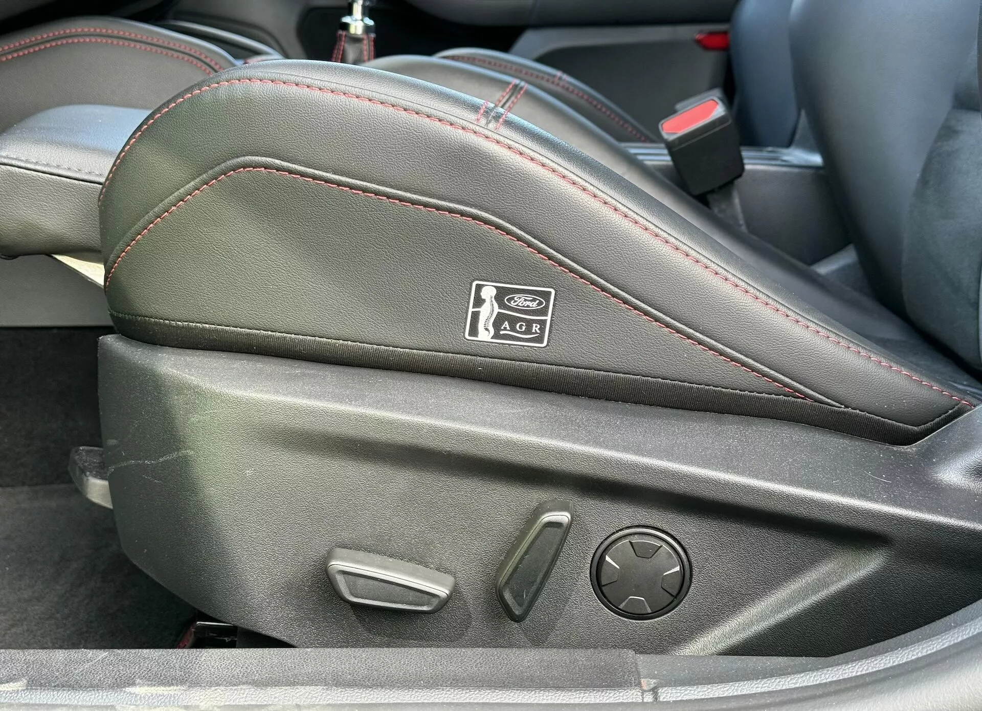 Primer plano del interior del Ford Focus ST 2022 enfocado en los controles laterales del asiento del conductor con ajuste electrónico y tapicería de cuero