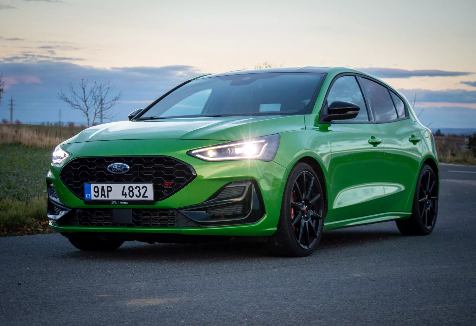 Ford Focus ST 2022 en verde vibrante, mostrando líneas de diseño y características desde un ángulo frontal bajo de tres cuartos, destacando los elegantes faros LED, rejilla frontal con logo central, parachoques deportivo con luces antiniebla e tomas de aire, spoiler delantero y detalles en negro sobre pintura metálica.
