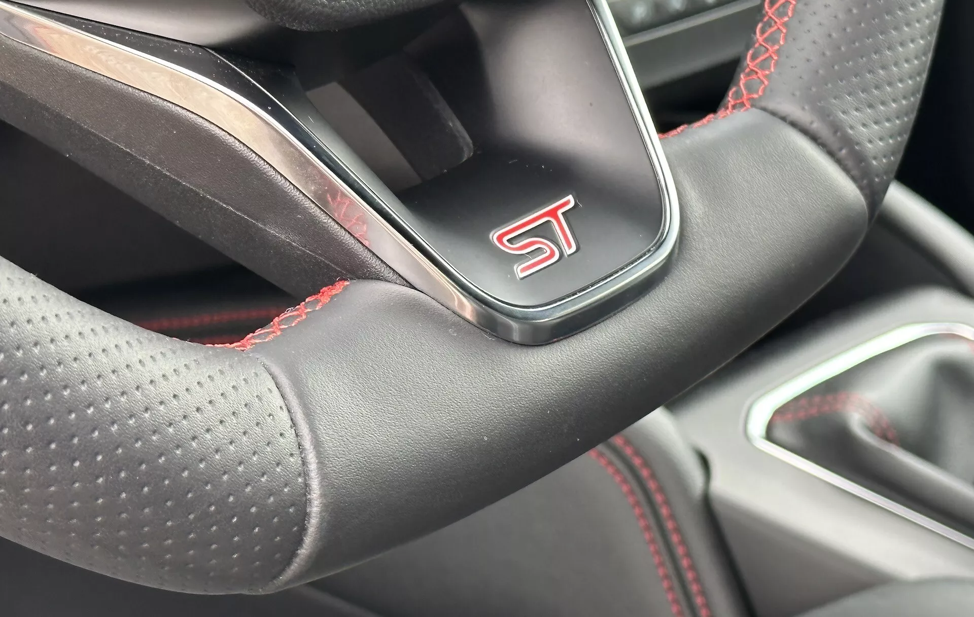 Vista cercana del volante del Ford Focus 2022 con diseño deportivo, cuero perforado, costuras en contraste rojo y logotipo 'ST', insinuando un modelo de rendimiento