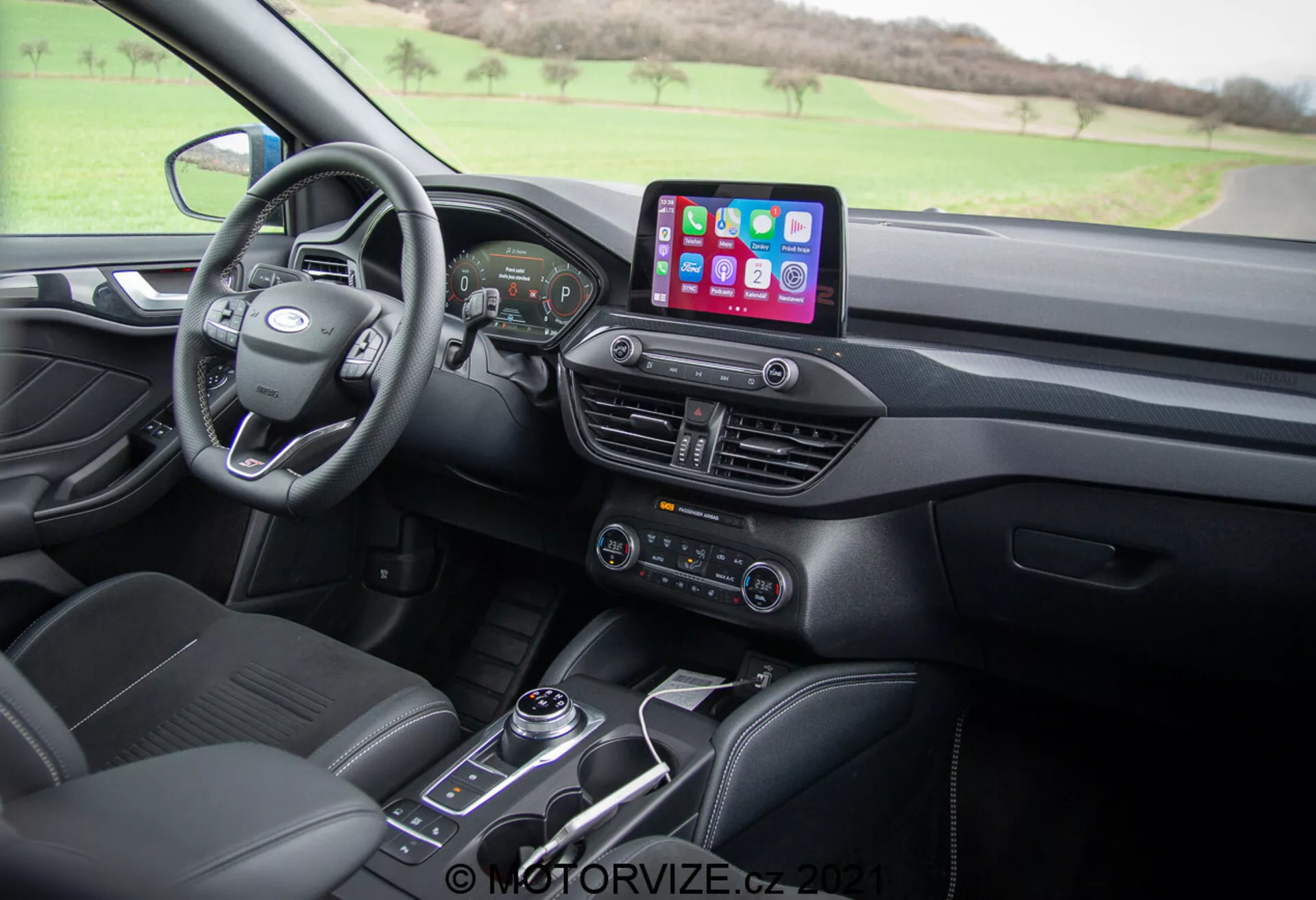 Vista del interior del Ford Focus 2022 desde el asiento del acompañante, que muestra un volante multifuncional moderno, tablero digital, sistema de infoentretenimiento con conectividad para smartphones como Apple CarPlay y Android Auto, sistema de control climático con botones para asientos calefaccionados, palanca de cambios automática y asientos de cuero con patrones de costura.