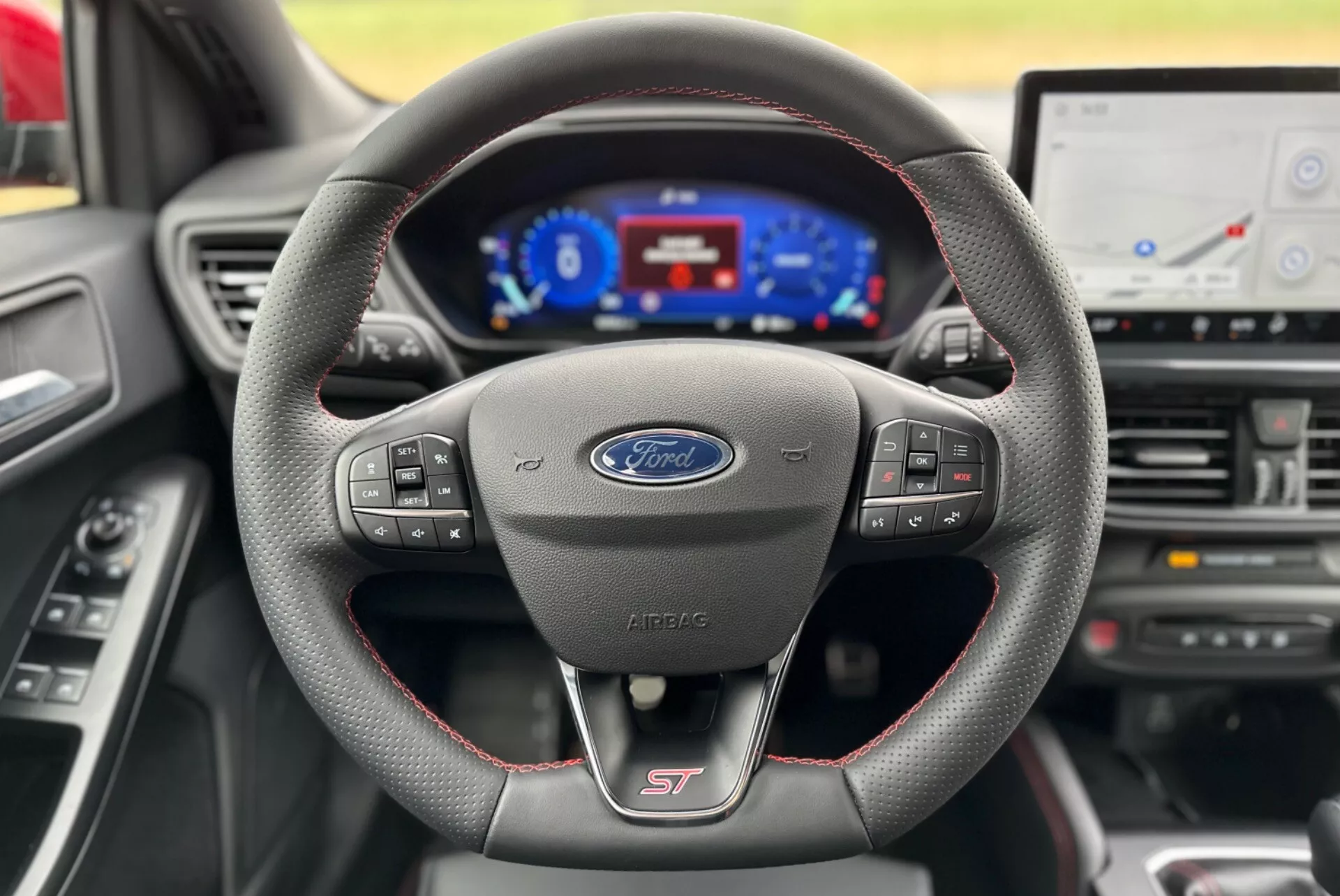 Vista interior del Ford Focus 2022 centrada en el volante deportivo forrado en cuero con costuras rojas y el logo ST, el cuadro de instrumentos digital y parte de la consola central con pantalla de infoentretenimiento