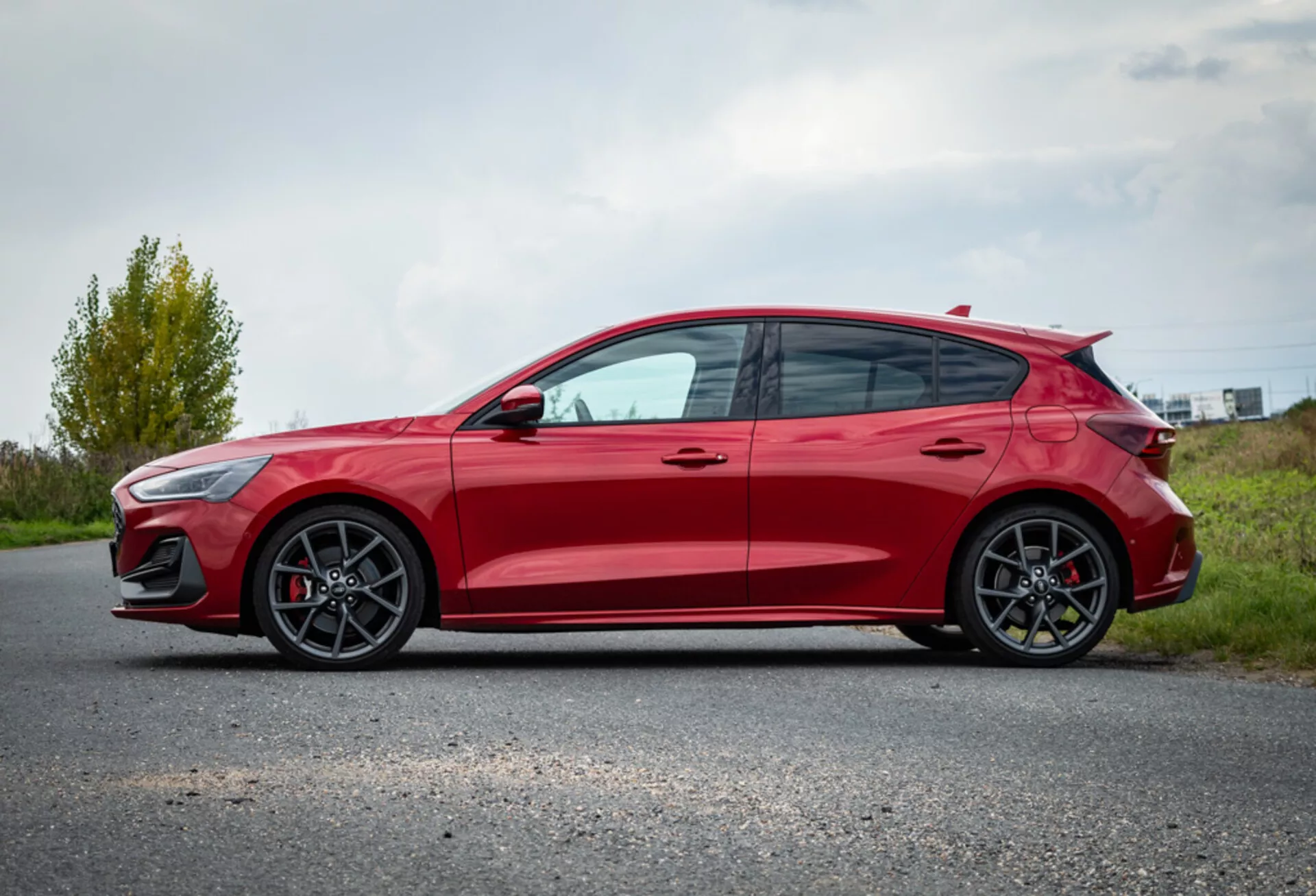 Coche hatchback Ford Focus rojo 2022 mostrando características de diseño desde un perfil lateral con ruedas de aleación, aerodinámica deportiva y aparcado en un camino pavimentado contra un fondo de paisaje natural