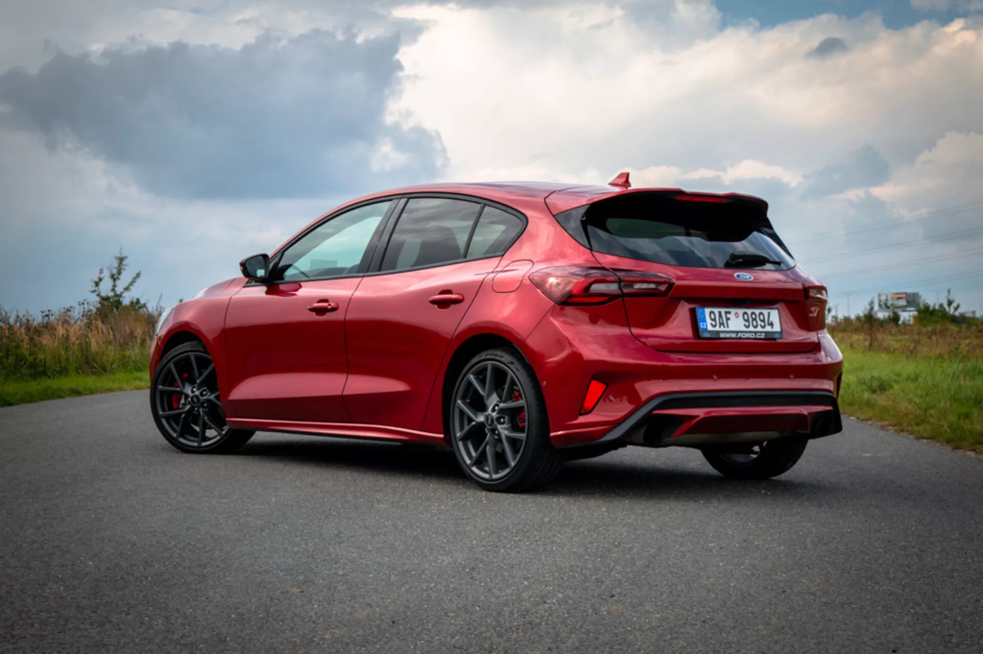 Hatchback rojo moderno Ford Focus 2022 capturado desde una vista trasera de tres cuartos mostrando diseño deportivo, aerodinámica optimizada, luces traseras LED, ruedas de aleación, alerón trasero y escape doble en carretera de asfalto