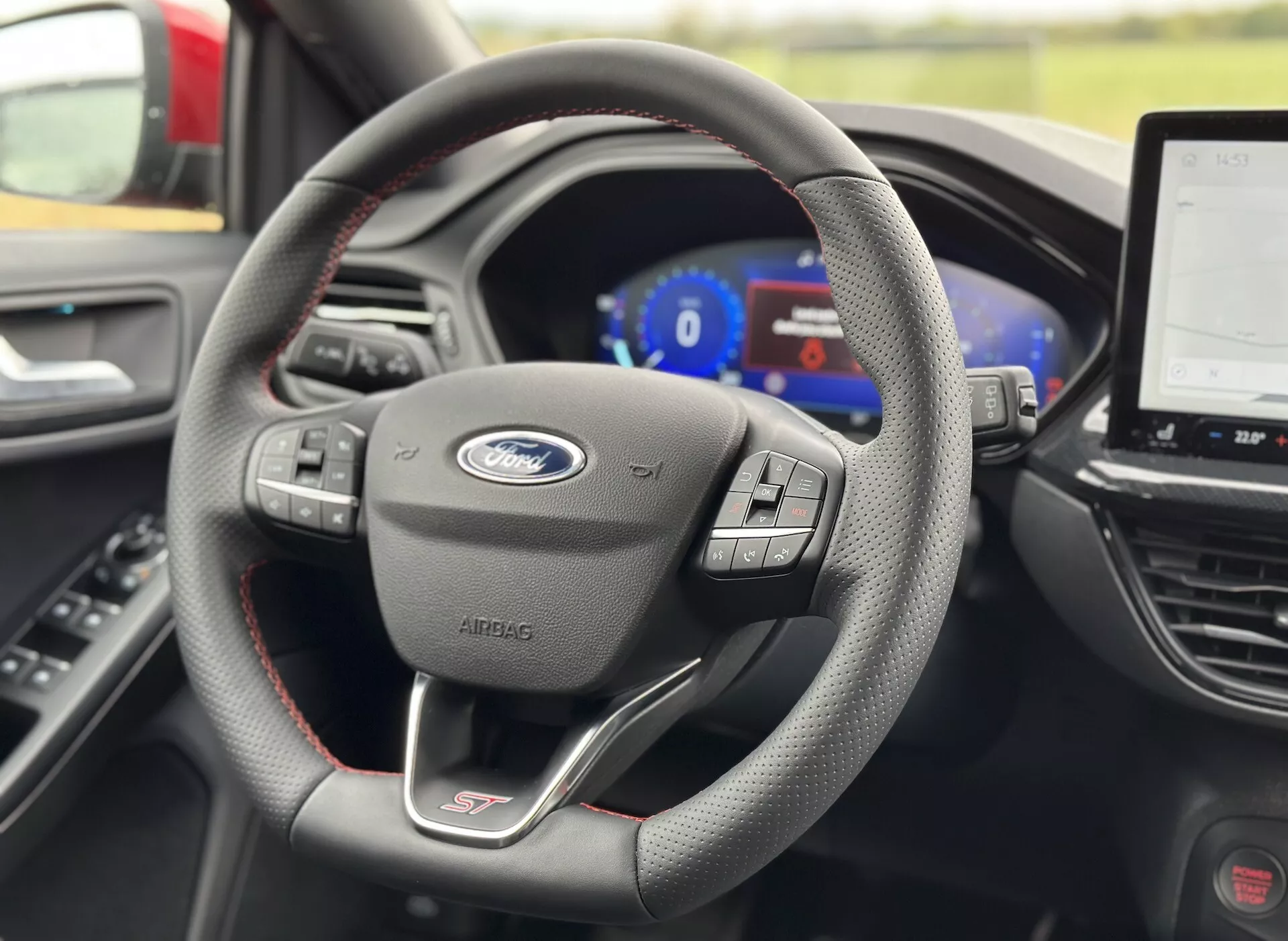 Vista interior del Ford Focus ST 2022 centrada en el volante con botones multifunción, levas de cambio y un cuadro de instrumentos digital con un sistema de infoentretenimiento táctil en el fondo.