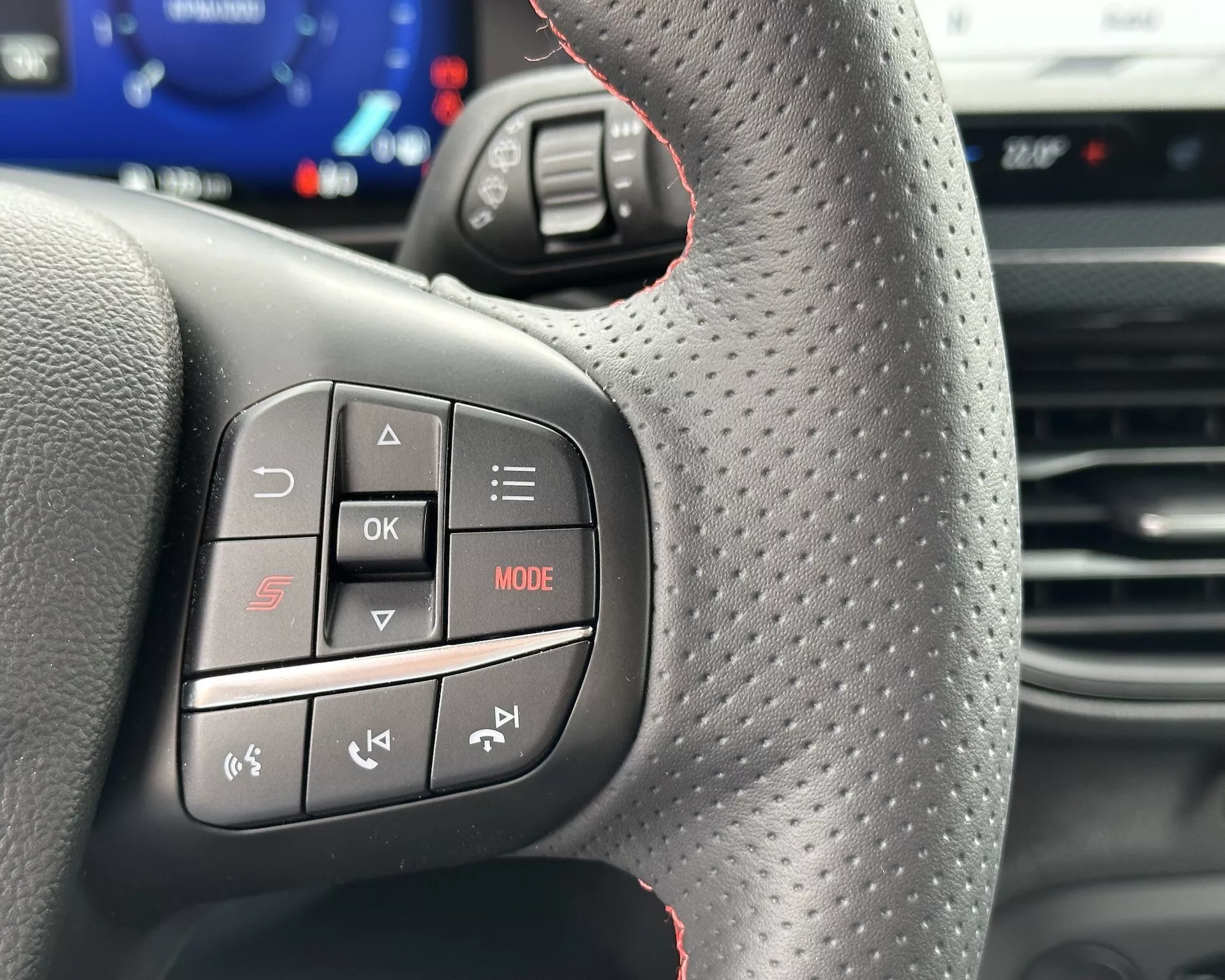 Vista en primer plano del volante del Ford Focus 2022 que muestra controles multifunción desde la perspectiva del conductor, con botones de audio y teléfono, costuras rojas deportivas y textura mejorada para el agarre.