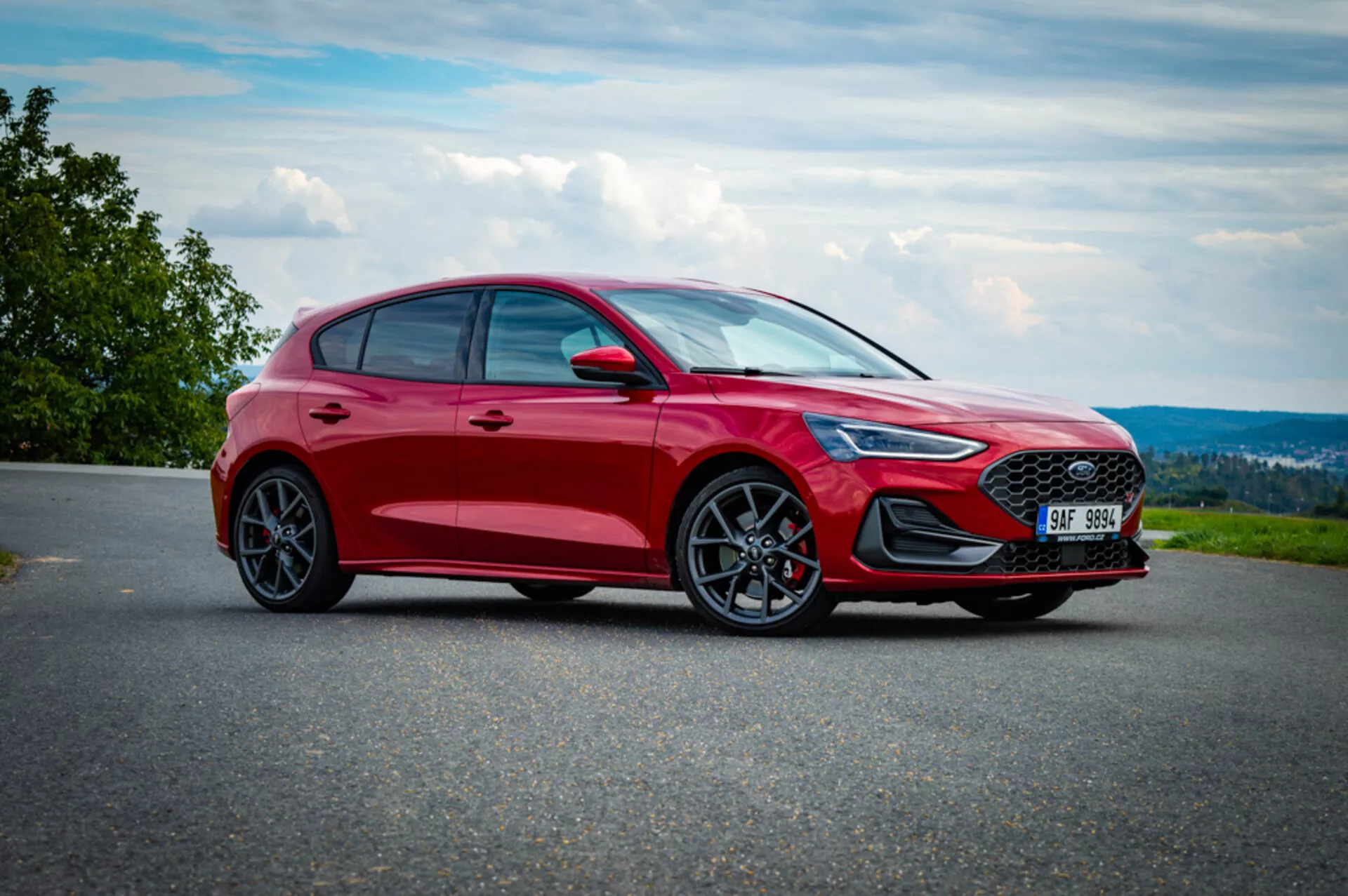 Vista frontal tres cuartos de Ford Focus hatchback rojo 2022 en una carretera pavimentada con fondo de campo, destacando su parrilla deportiva, faros LED, parachoques esculpido, ruedas de aleación y perfil dinámico.