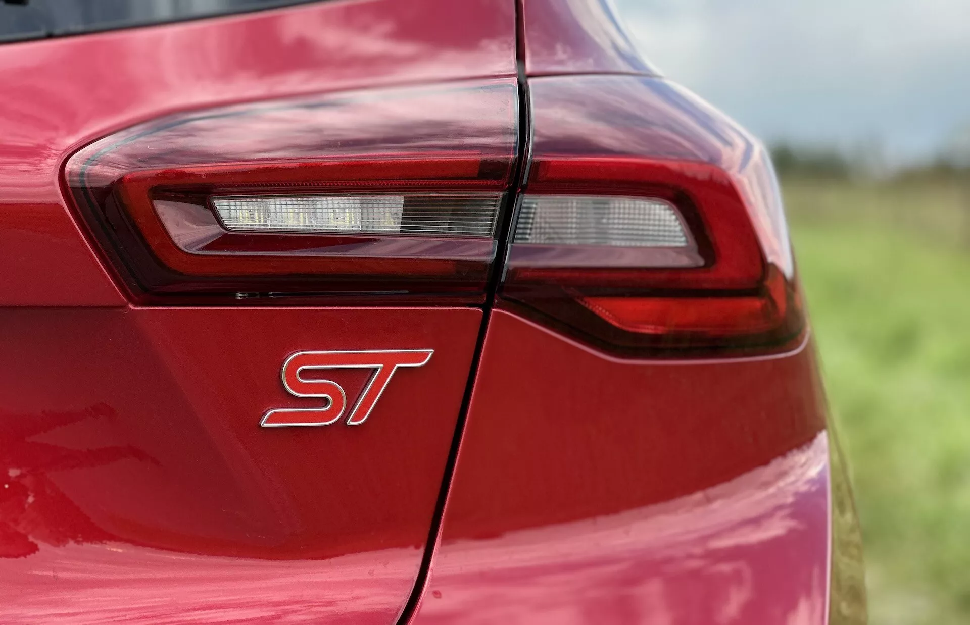 Primer plano del cuarto trasero del Ford Focus ST 2022 mostrando carrocería roja vibrante, insignia de afinación deportiva y diseño de luz trasera LED