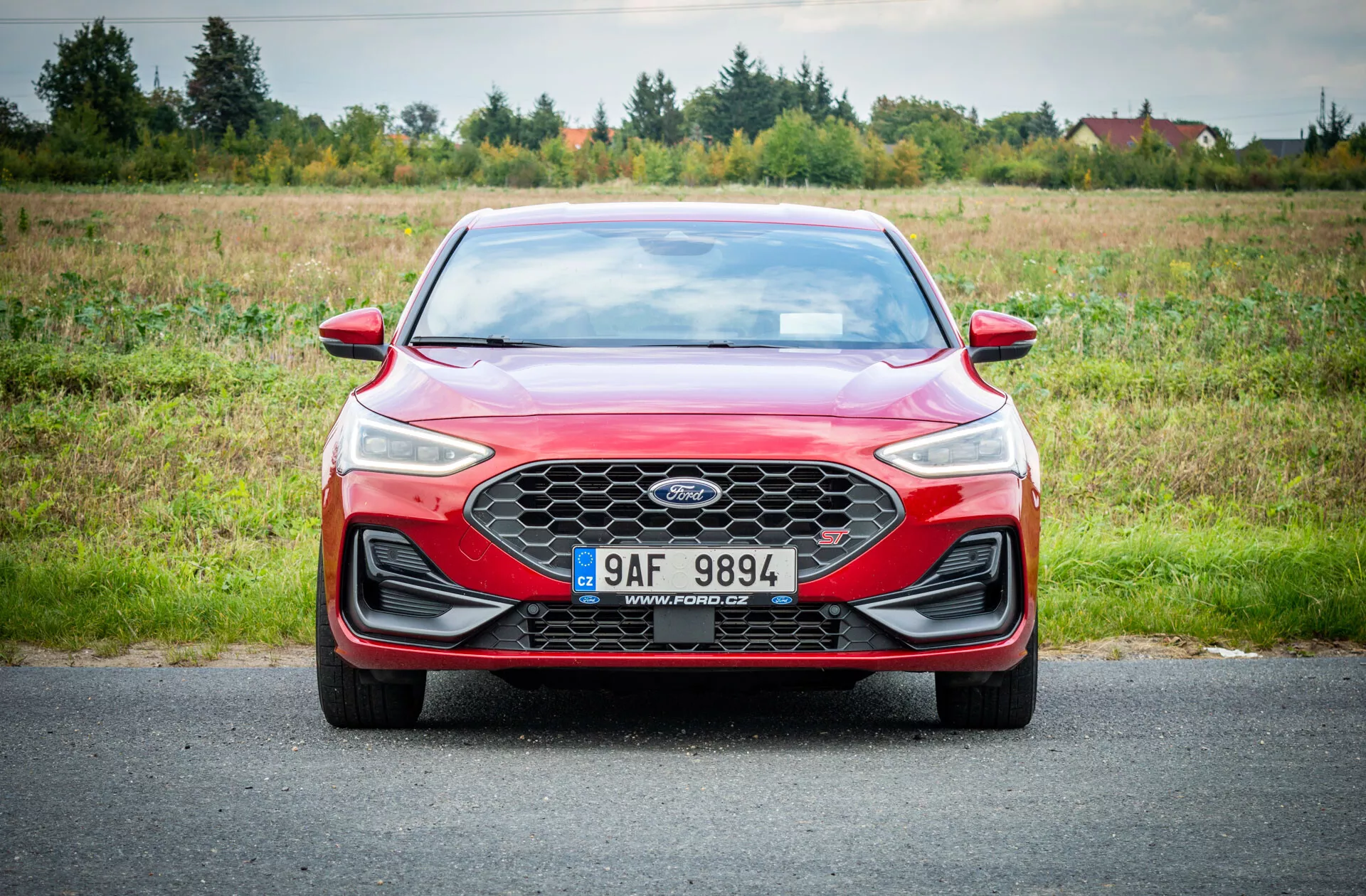 Sedán rojo Ford Focus 2022 sobre carretera con fondo natural de pasto bajo iluminación nublada mostrando vista frontal con parrilla de panal, faros LED y diseño aerodinámico