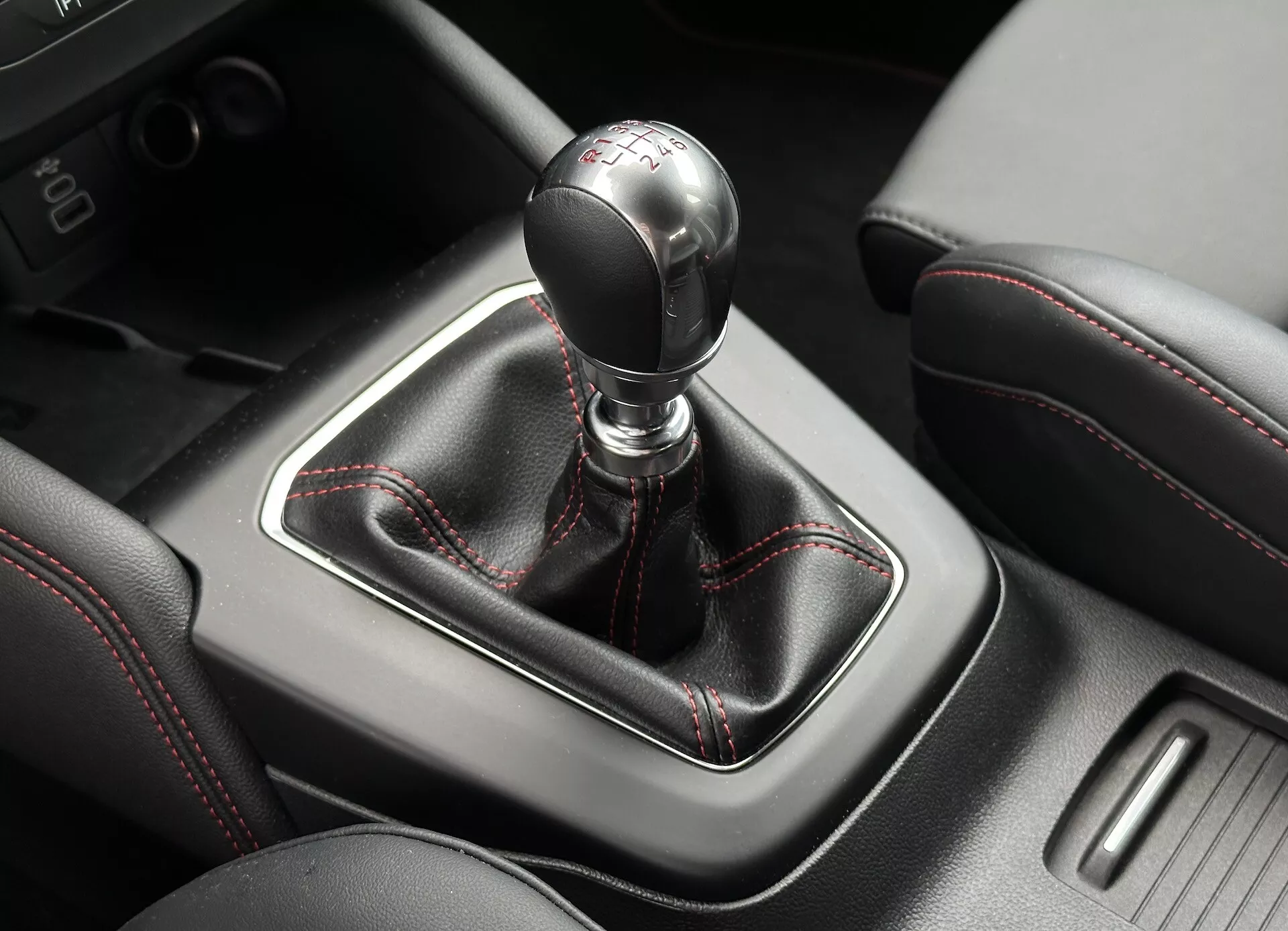 Vista detallada de la palanca de cambios manual del Ford Focus 2022 con costuras rojas, detalles en cuero y consola circundante
