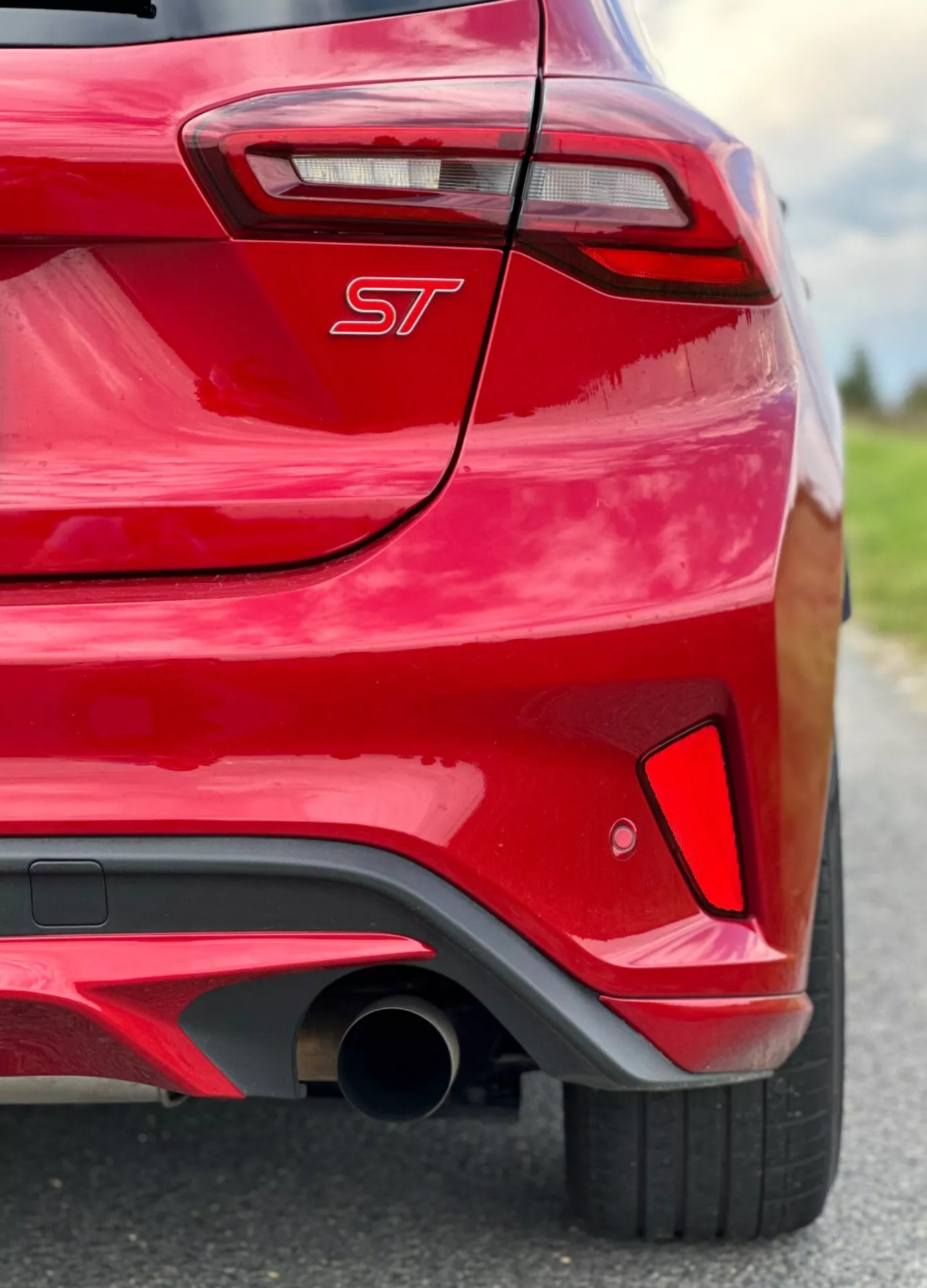 Vista angular cercana de la sección trasera de un Ford Focus 2022 en rojo, mostrando el diseño y la marca con un emblema ST, parte de la elegante luz trasera LED y un tubo de escape orientado al rendimiento integrado en el parachoques con un difusor negro.