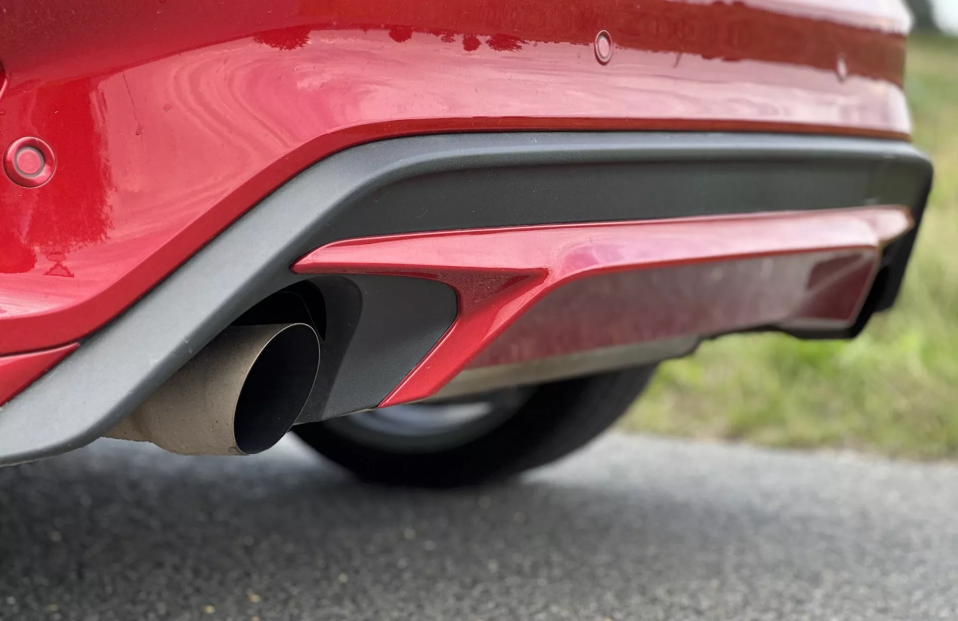 Primer plano de la sección trasera inferior de un Ford Focus 2022 mostrando un parachoques rojo brillante, un tubo de escape metálico, diseño aerodinámico deportivo y sensores de estacionamiento reflectantes