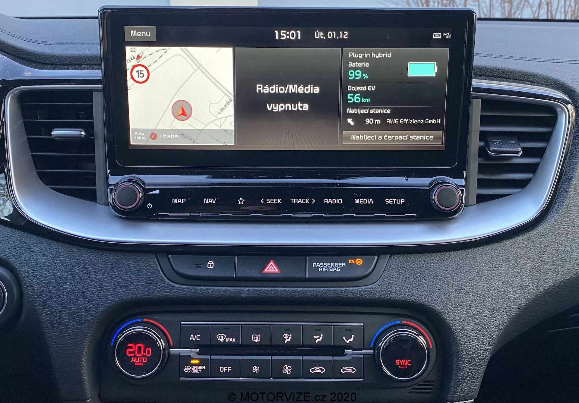 Perspectiva en primera persona de la consola central y el sistema de infoentretenimiento del Kia Ceed 2018, que presenta una pantalla a color que muestra información de navegación y medios, botones físicos para control y un panel de control climático con pantalla digital y diversas funcionalidades.