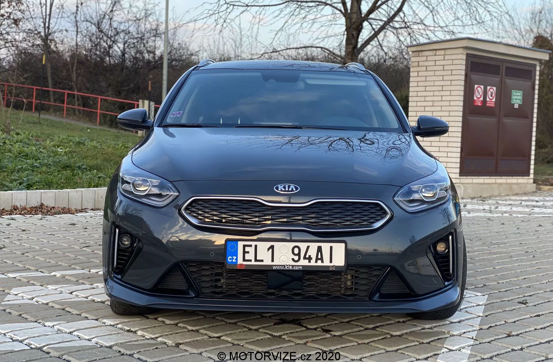 Vista frontal de un coche Kia Ceed 2018 desde un ángulo bajo, mostrando características frontales como la rejilla, los faros y el parachoques con una estética moderna. La imagen destaca el emblema plateado de Kia en una rejilla negra texturizada, los faros horizontales elegantes y el parachoques delantero con grandes entradas de aire, lo que sugiere características de rendimiento deportivo o refrigeración avanzada por flujo de aire.