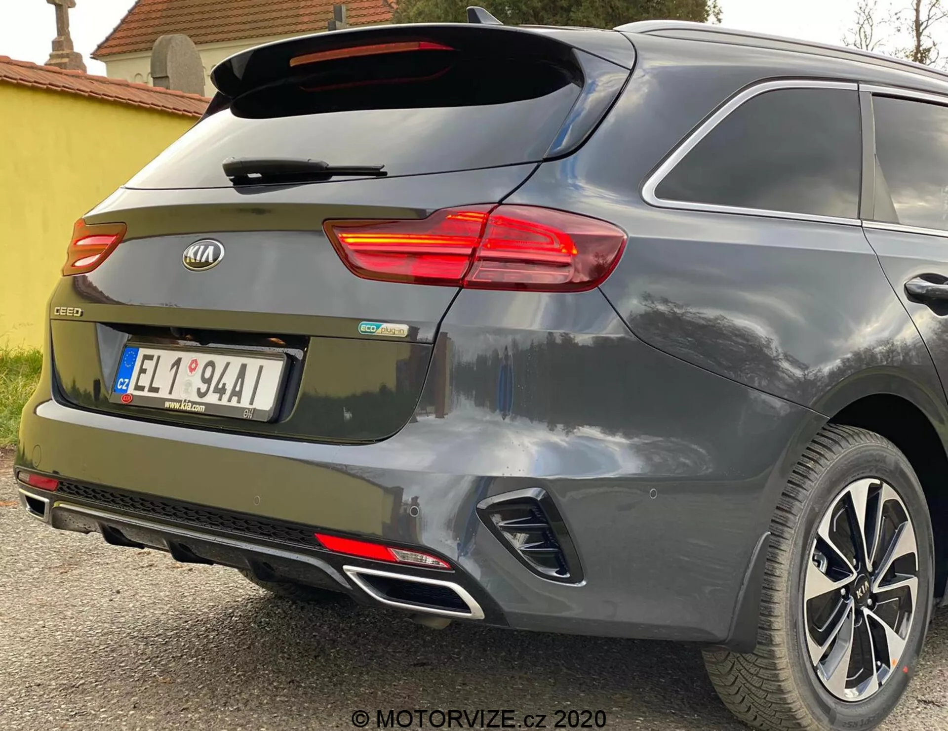 Vista parcial en ángulo trasero de un Kia Ceed 2018, destacando la luz trasera derecha iluminada, el parabrisas trasero con limpiaparabrisas, el portón trasero con el emblema de la marca y la insignia del modelo 'CEED', reflectores integrados en el parachoques trasero, sensores de estacionamiento, sistema de escape dual y llantas de aleación contra una pintura gris metálica o plateada.
