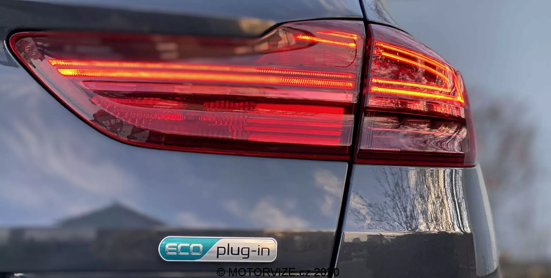 Vista de cerca del lado trasero izquierdo de un Kia Ceed 2018, centrada en el conjunto de luces traseras iluminadas con un diseño en varias capas. La insignia 'ECO plug-in' indica que es un vehículo híbrido enchufable. El acabado brillante y la tapa del maletero ligeramente visible añaden detalles al diseño general del coche.