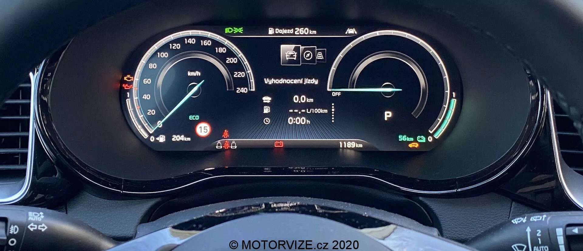 Vista de primer plano del cuadro de instrumentos digital del Kia Ceed 2018 tomada desde el asiento del conductor. La pantalla incluye un velocímetro con una aguja física y una lectura digital que muestra 15 km/h. A la derecha, hay un medidor de energía/batería que indica una batería llena con un alcance de 481 km. Otros elementos incluyen una pantalla de estado de listo, información del conductor con luces de advertencia, una lectura de temperatura externa de 20.5°C y el vehículo en modo Park. El arco superior del volante, con un diseño deportivo y fondo plano, es visible.