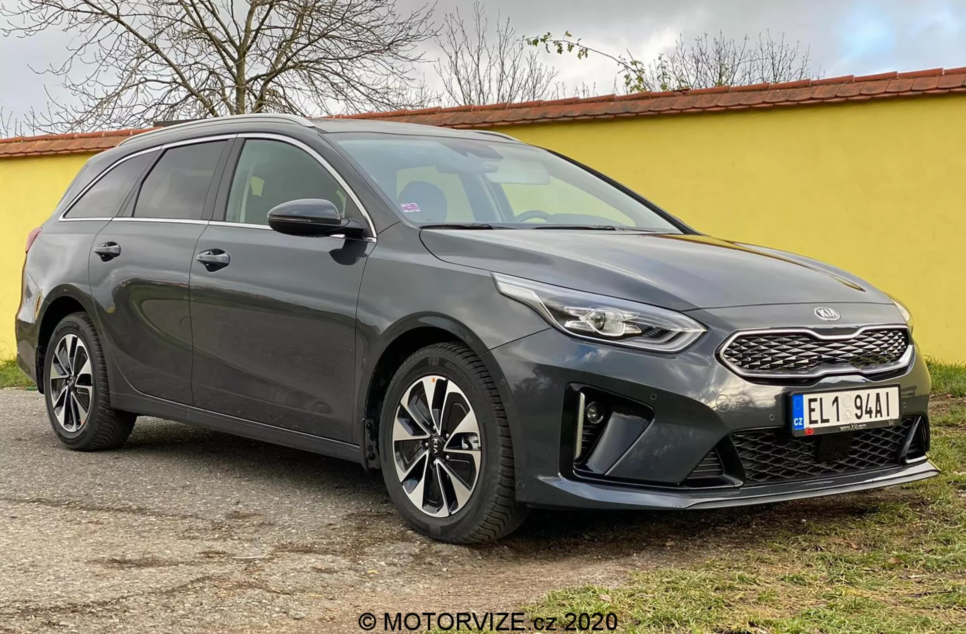 La imagen muestra el Kia Ceed 2018, una moderna camioneta capturada desde un ángulo de tres cuartos frontal, destacando su fascia delantera que incluye una parrilla estructurada con un emblema distintivo de la marca, faros estrechos que se extienden hacia atrás con luces LED diurnas y un parachoques delantero con carcasas de luces antiniebla y sensores de aparcamiento. Las elegantes líneas de contorno del capó conducen a un parabrisas inclinado, acentuando el perfil aerodinámico del coche. Son visibles las llantas de aleación de múltiples radios y los espejos laterales con intermitentes integrados, junto con una línea de techo descendente hacia la parte trasera y los rieles del techo, lo que enfatiza tanto el estilo como la utilidad. Las ventanas tintadas y las líneas de la carrocería a lo largo del lateral añaden una apariencia esculpida. El coche está estacionado sobre una superficie plana al aire libre.