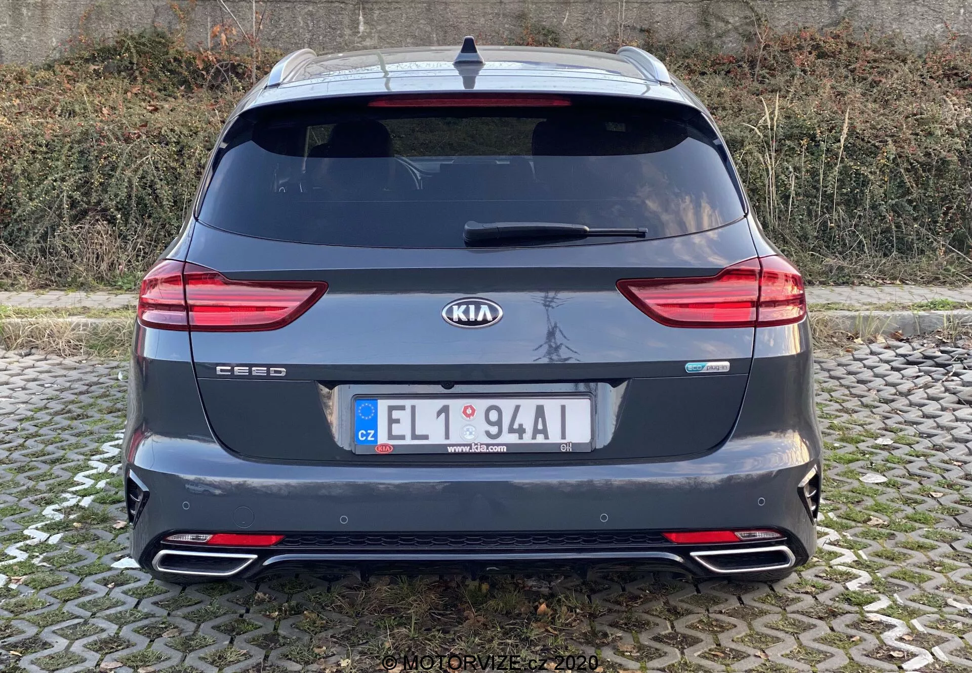 Vista trasera de un Kia Ceed 2018 mostrando toda la sección trasera con insignias de marca y modelo, luces traseras LED modernas, ventana trasera, doble salida de escape, parachoques trasero con reflectores, alerón de techo, antena y sensores de aparcamiento traseros. La imagen es clara, tomada a nivel de los ojos con luz natural en condiciones de cielo nublado.