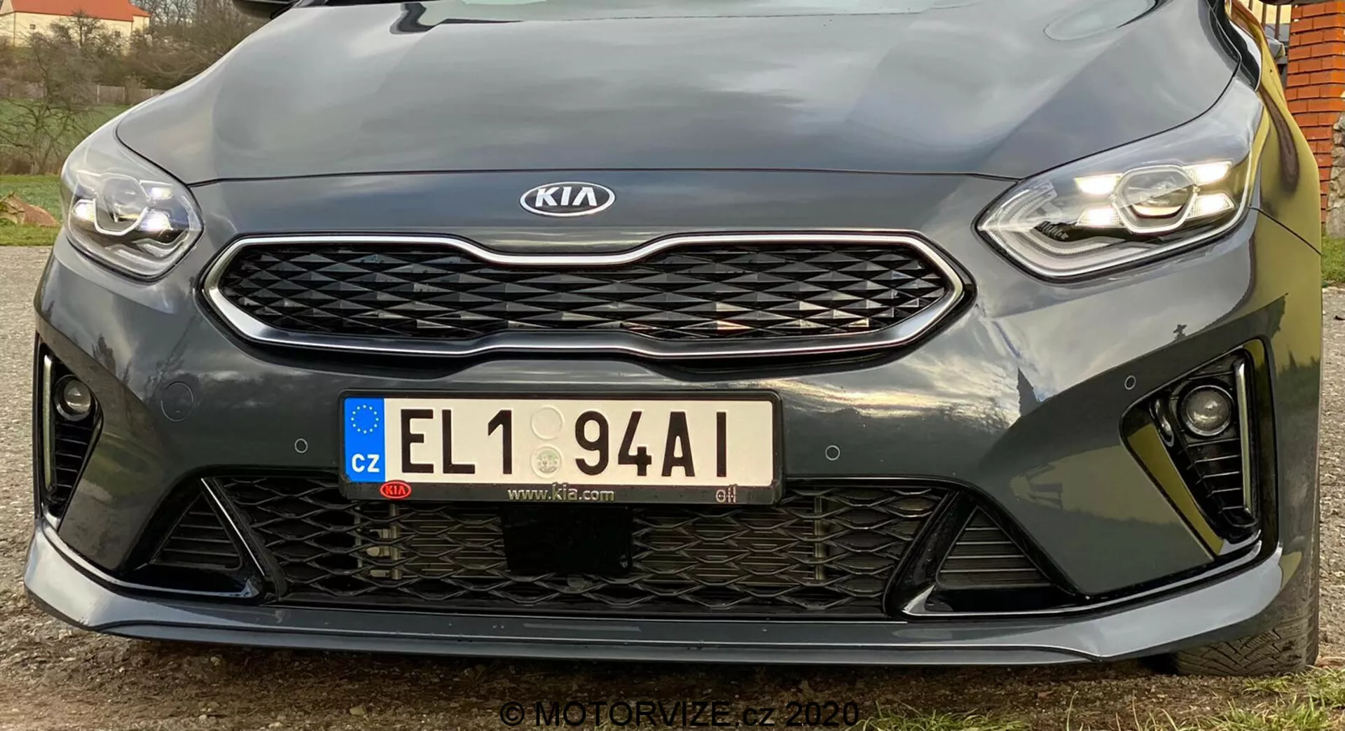 Esta imagen muestra la parte frontal de un Kia Ceed 2018 tomada desde un ángulo bajo. Destaca los faros LED horizontales y elegantes, la parrilla prominente con patrón de panal y el emblema de Kia centrado, la placa de matrícula europea de la República Checa y el parachoques delantero deportivo con grandes aperturas. La vista cercana resalta los sensores de estacionamiento debajo de la parrilla. El diseño deportivo sugiere un nivel de acabado de mayor rendimiento, aunque las especificaciones exactas no son claras. La imagen de alta resolución captura detalles de diseño y contornos, con un ángulo descentrado hacia la izquierda.