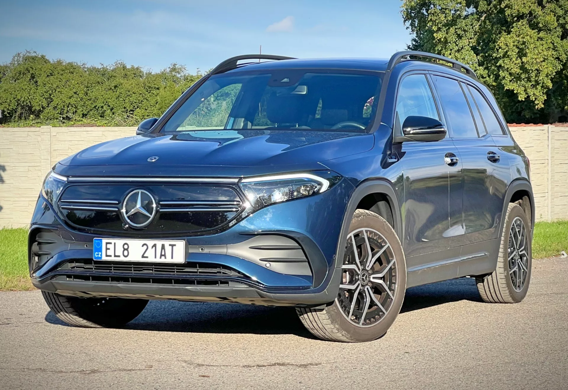 Vista frontal tres cuartos dinámica del Mercedes-Benz EQB 2021 mostrando su altura y postura con características como parrilla frontal con emblema, faros LED, grandes ruedas de aleación, parachoques delantero deportivo, capó contorneado para aerodinámica, espejos con señales de giro integradas, línea de carácter para una mirada dinámica, barras de techo para utilidad adicional y ventanas tintadas para privacidad, en un día soleado