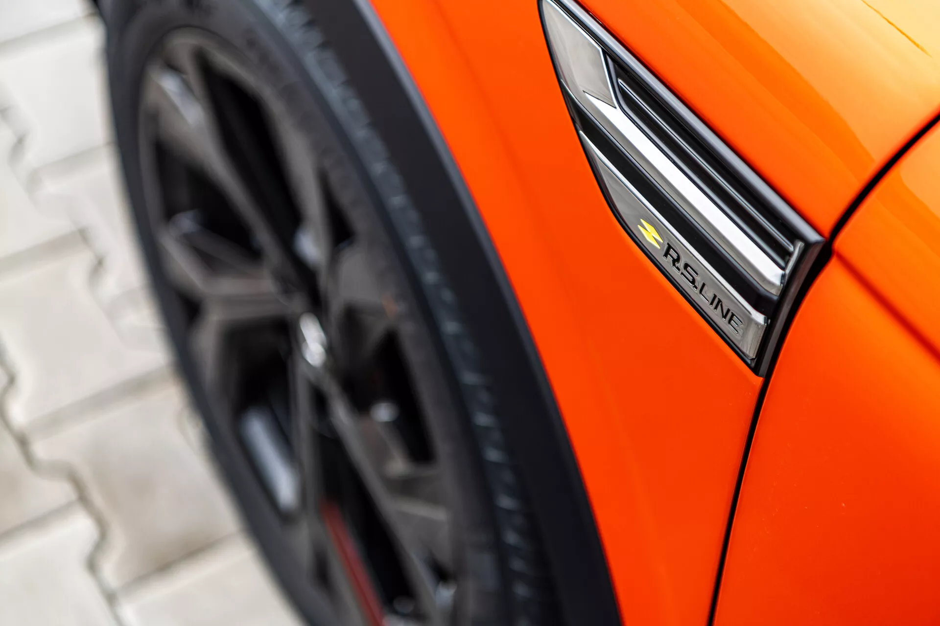 Vista cercana de un Renault Arkana naranja del 2021 mostrando el perfil lateral con enfoque en la insignia S-Line, guardabarros y diseño de rueda deportiva desde un ángulo bajo