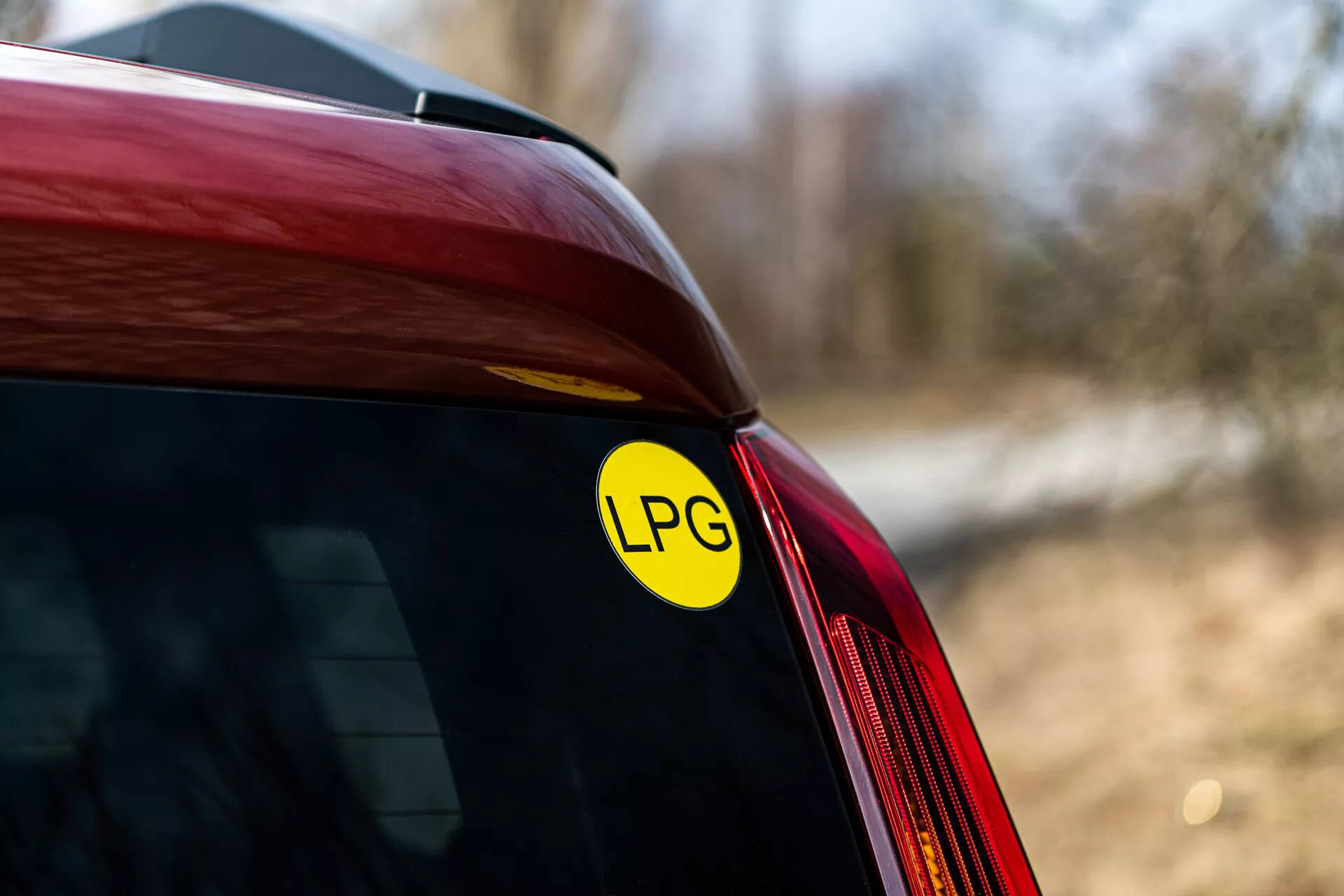 Primer plano de la esquina trasera de un Renault Arkana rojo de 2021 mostrando la pegatina de GLP para la capacidad de gas licuado de petróleo, con enfoque en la unión del parabrisas trasero y el panel lateral, bajo luz natural al aire libre
