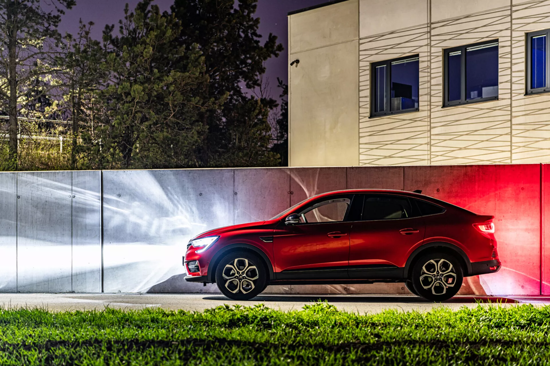 Vista lateral del Renault Arkana 2021 por la noche, destacando su elegante color rojo, diseño deportivo y características avanzadas contra un fondo urbano estilizado