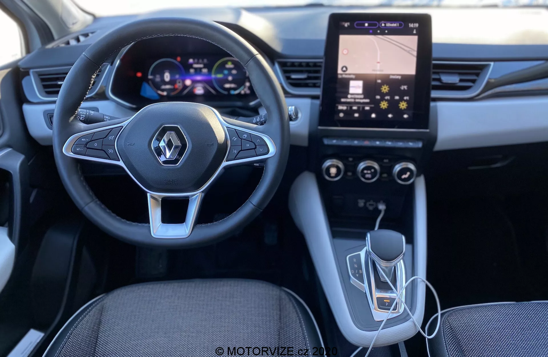 Imagen del interior del Renault Captur 2020 desde la perspectiva del conductor, destacando el volante de diseño moderno con controles multimedia integrados, el cuadro de instrumentos digital, el sistema de infoentretenimiento con pantalla táctil vertical y controles HVAC, la palanca de cambios automática y la conectividad USB. La iluminación y la calidad sugieren un interior bien diseñado y tecnológicamente avanzado.